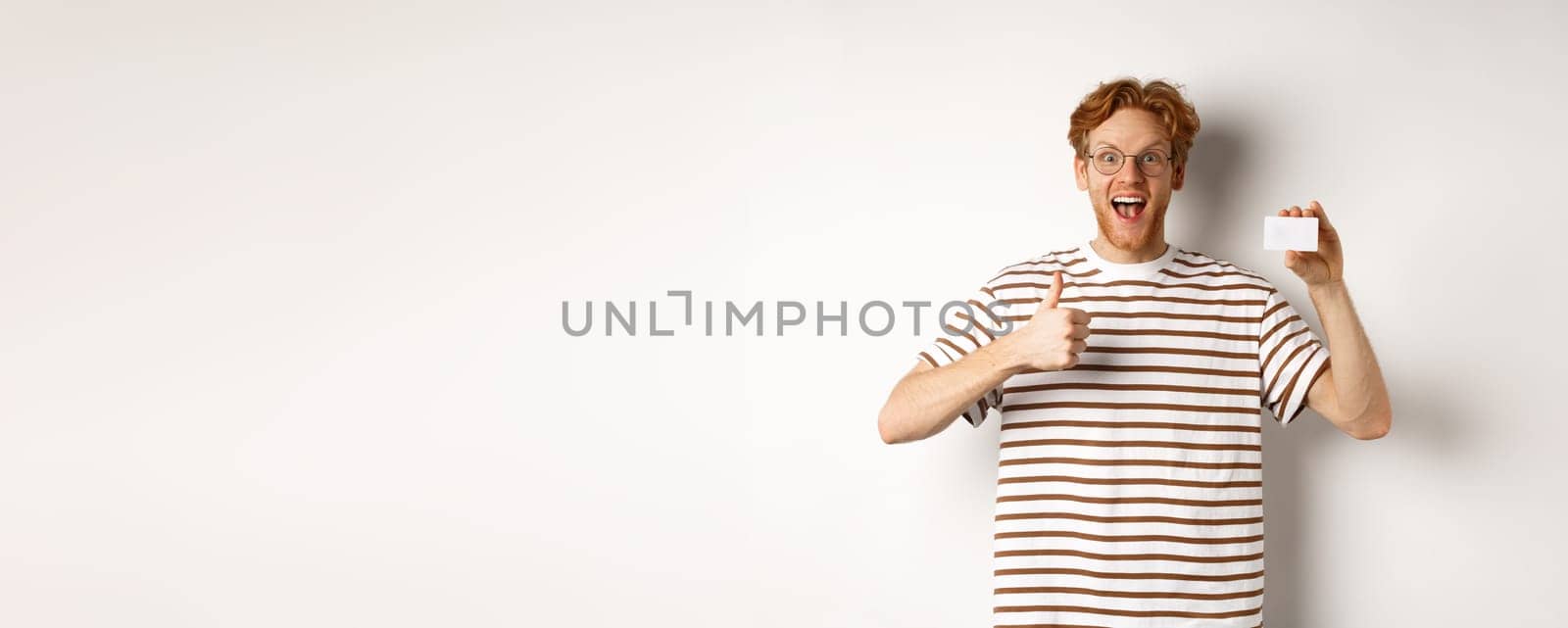 Shopping and finance concept. Satisfied male bank client showing thumbs-up and plastic credit card, smiling happy at camera by Benzoix