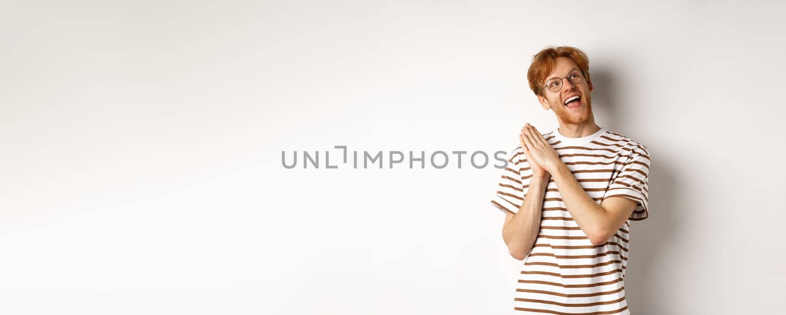 Happy redhead man clap hands and looking satisfied at upper right corner, getting ready for something, standing over white background.