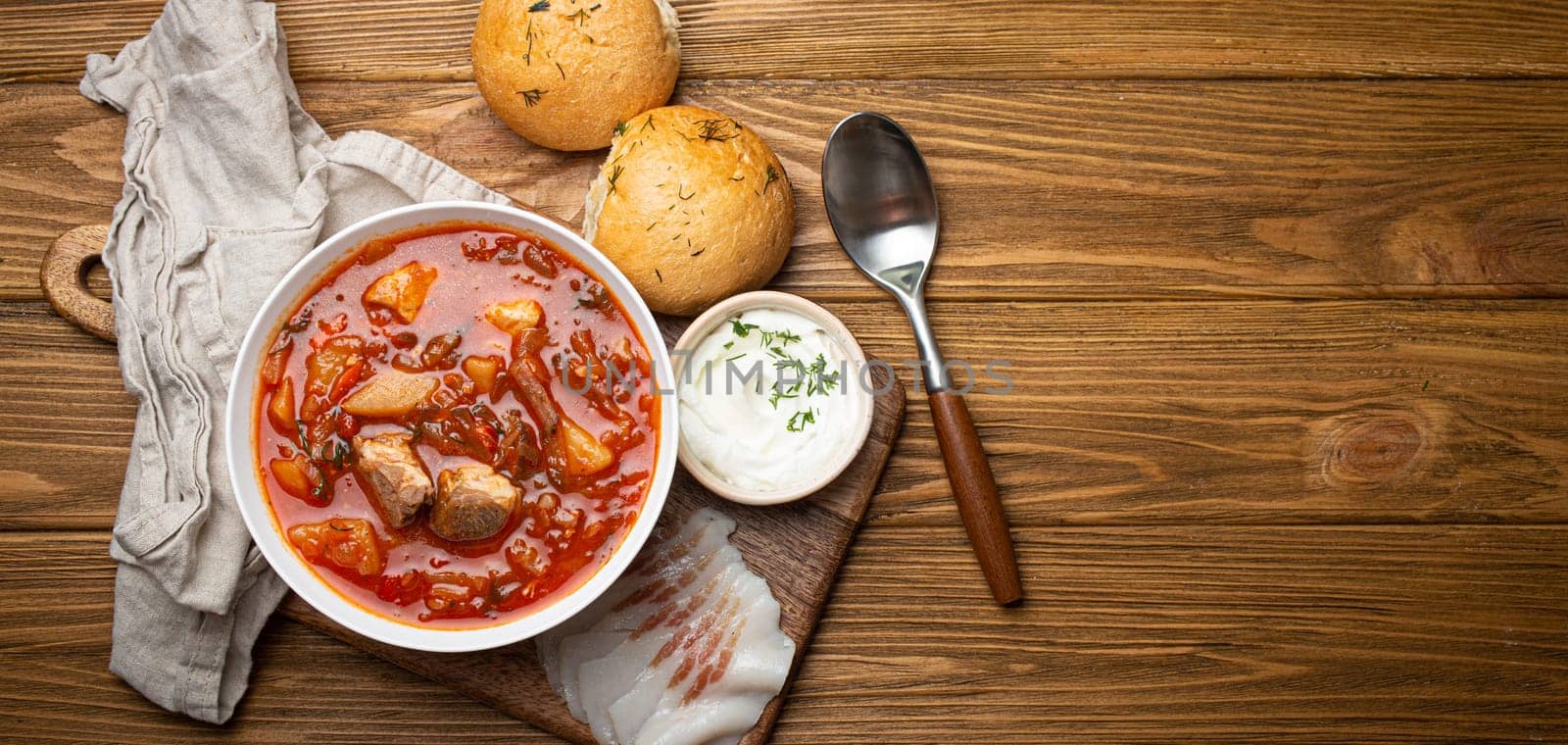 Ukrainian Borscht, red beetroot soup with meat, in white bowl with sour cream, garlic buns Pampushka and salo slices on rustic stone background. Traditional authentic dish of Ukraine, space for text