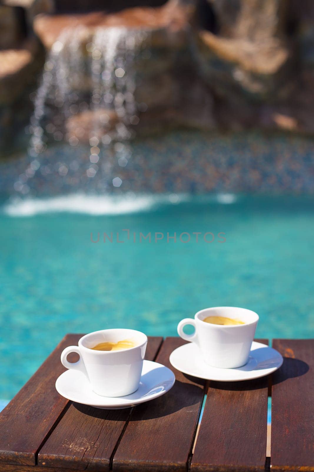 Two cups of coffee on the table near the pool.