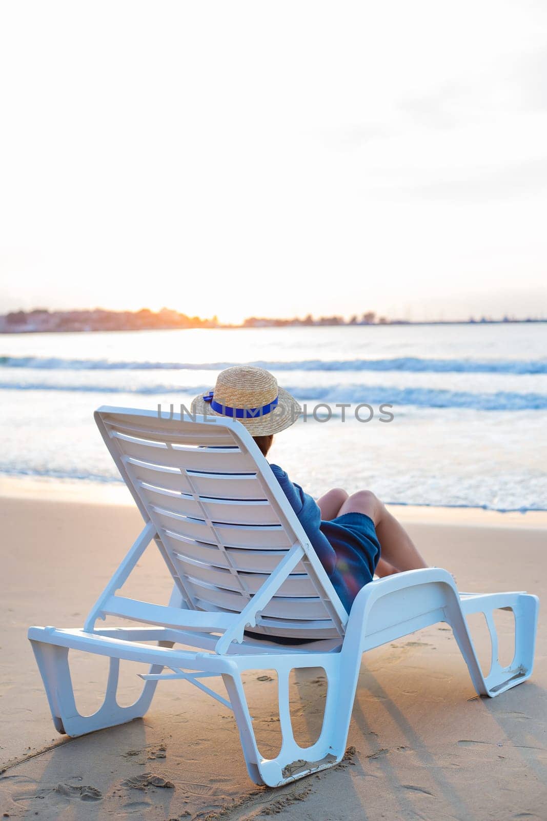 Beautiful girl in a hat sits on a deckchair meeting the dawn by sfinks