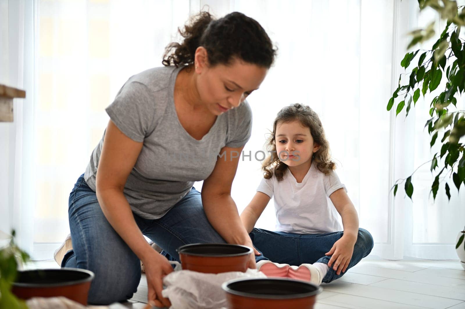 Selective focus: mom and daughter planting seeds and repotting houseplants at springtime by artgf