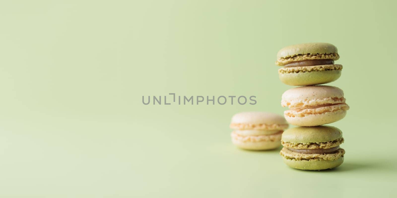 Vanilla and pistacio pastel colored eco handmade macaroons on green background. Gift for 8 March, International Women's Day, Valentine Day. Horizontal banner with copyspace