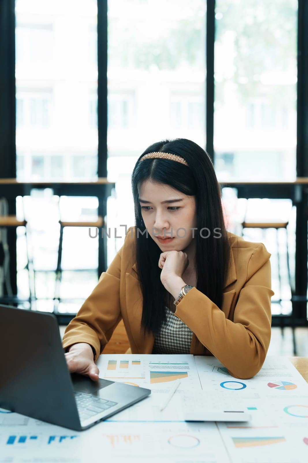 Portrait of a thoughtful Asian businesswoman looking at financial statements and making marketing plans using a computer on her desk.