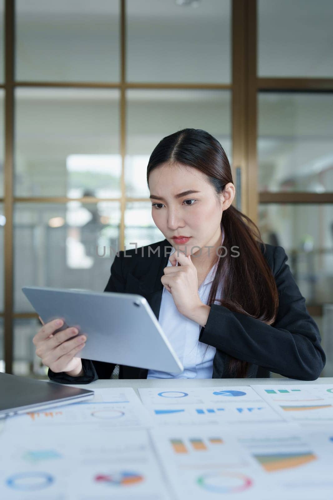 Portrait of a thoughtful Asian businesswoman looking at financial statements and making marketing plans using a tablet computer on her desk.