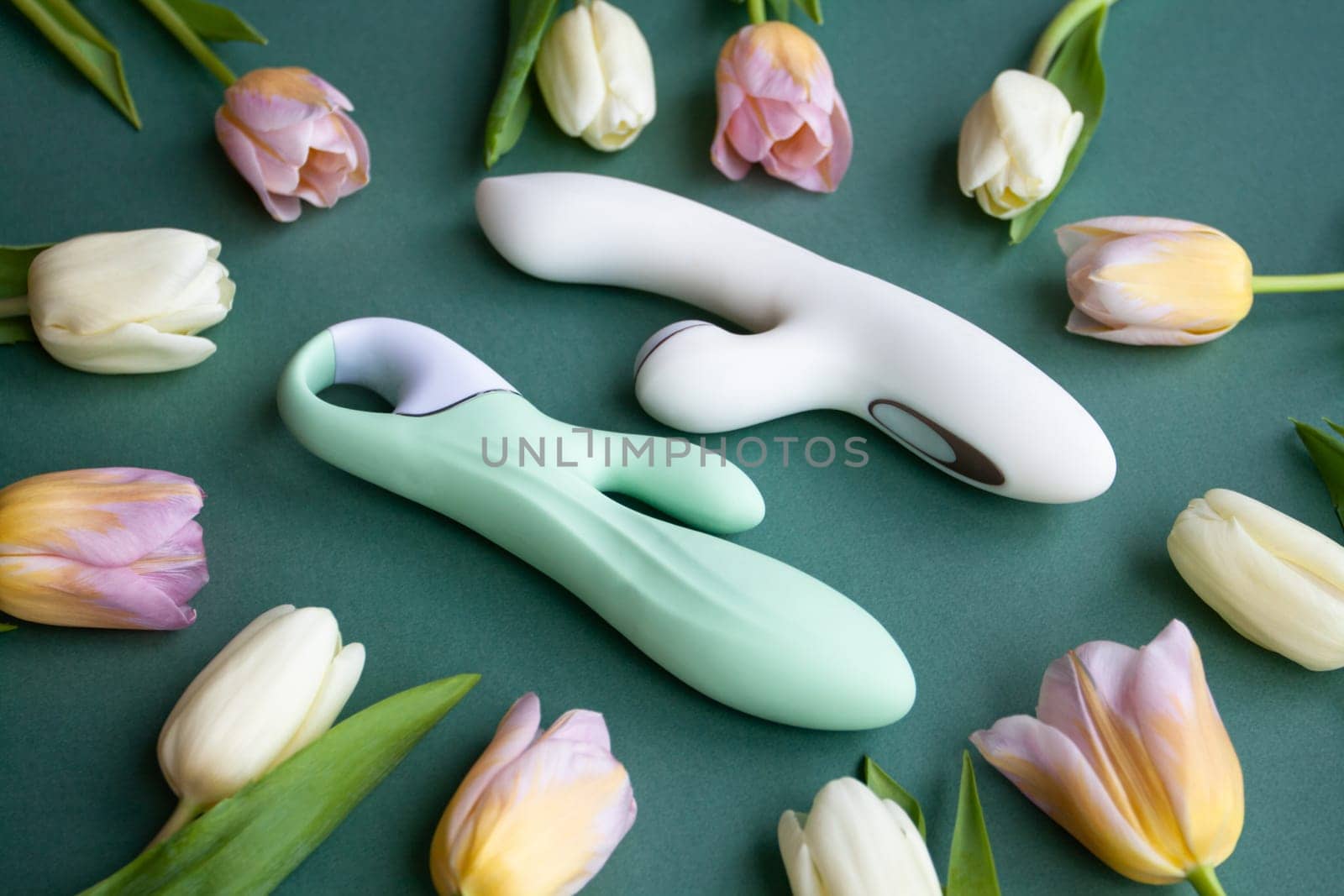 Two toys for adults lie on a green background, surrounded by tulips