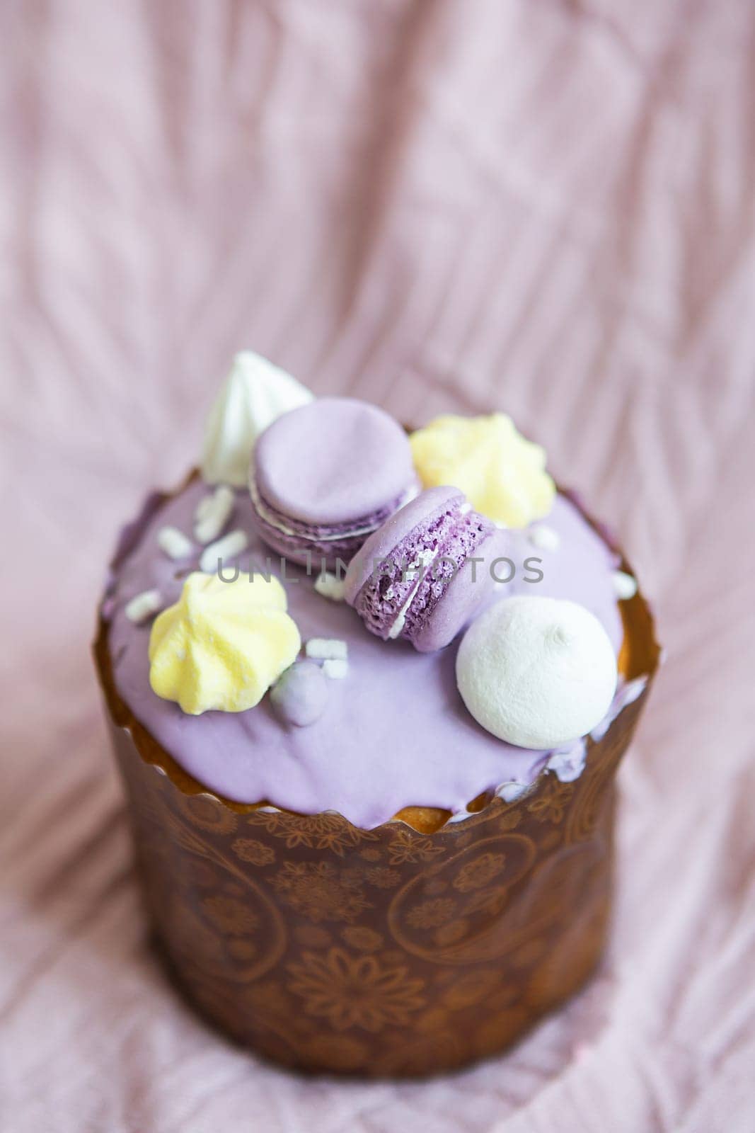 A traditional paska decorated with white Swiss chocolate and meringue stands on a lavender tablecloth. Easter holiday
