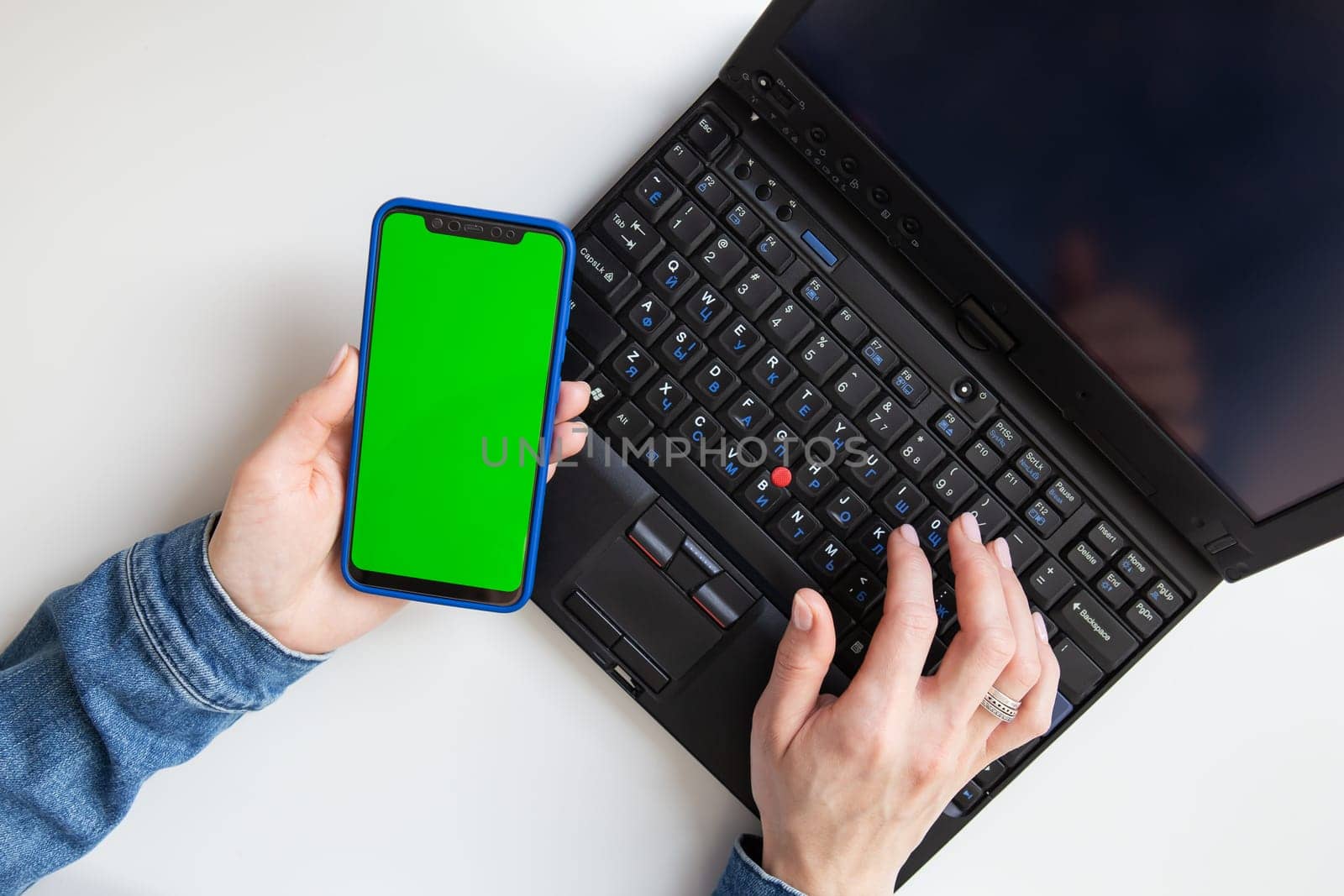 The girl is working on a laptop. Freelance, remote work, hands on the keyboard, in one hand a smartphone with a green screen. Mocap. View from above