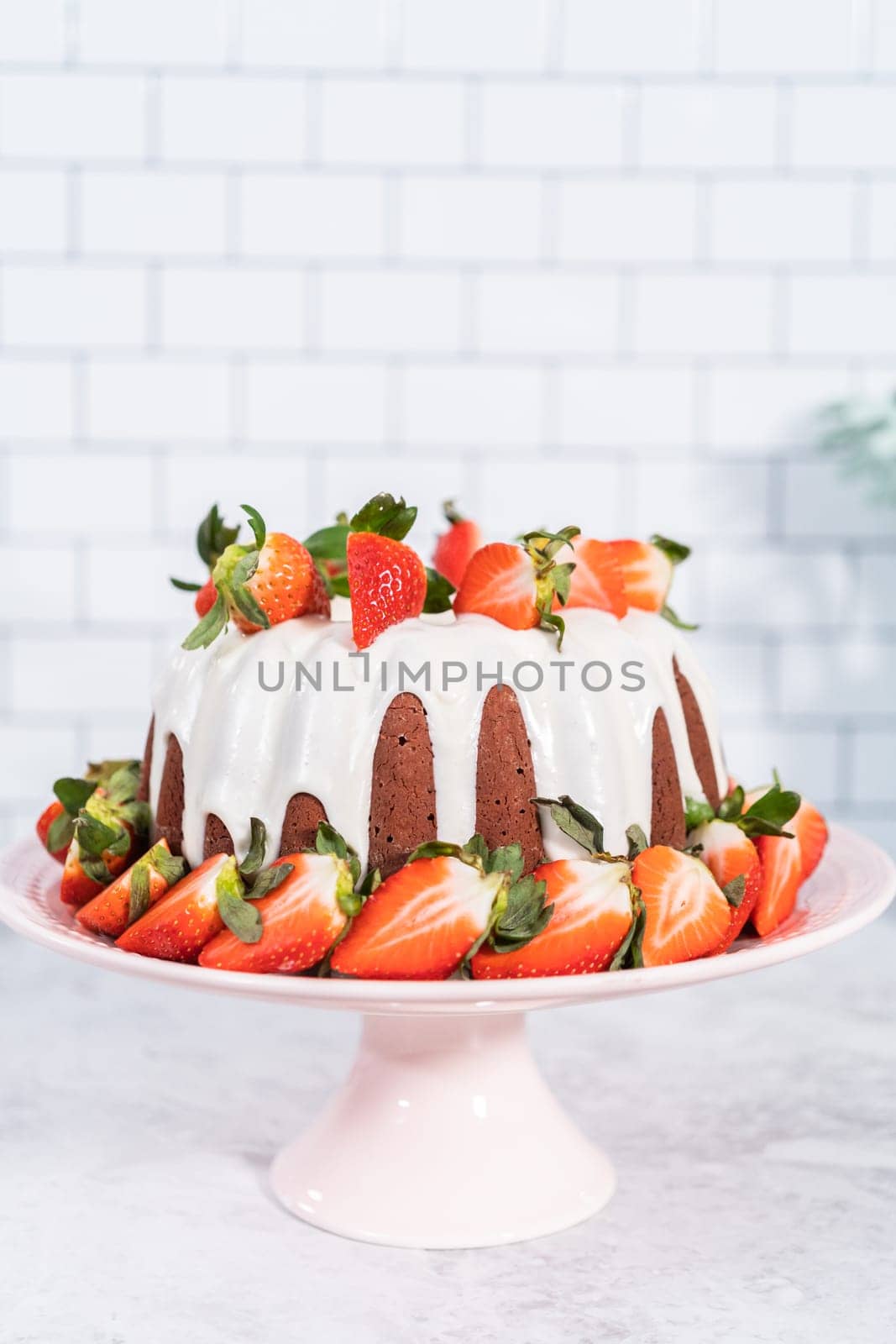 fresh strawberries..Red velvet bundt cake with cream cheese frosting garnished with fresh strawberries on a pink cake stand for Valentines Day.