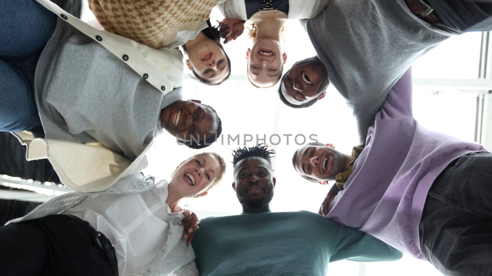 Closeup portrait, bottom view, happy faces of different team employees standing in circle, looking at camera, smiling business women and businessmen doing team building, posing for photo