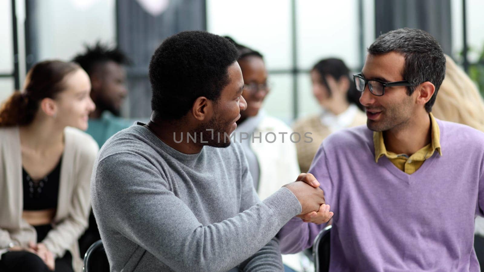 Diverse people sitting in circle holding hands at group therapy