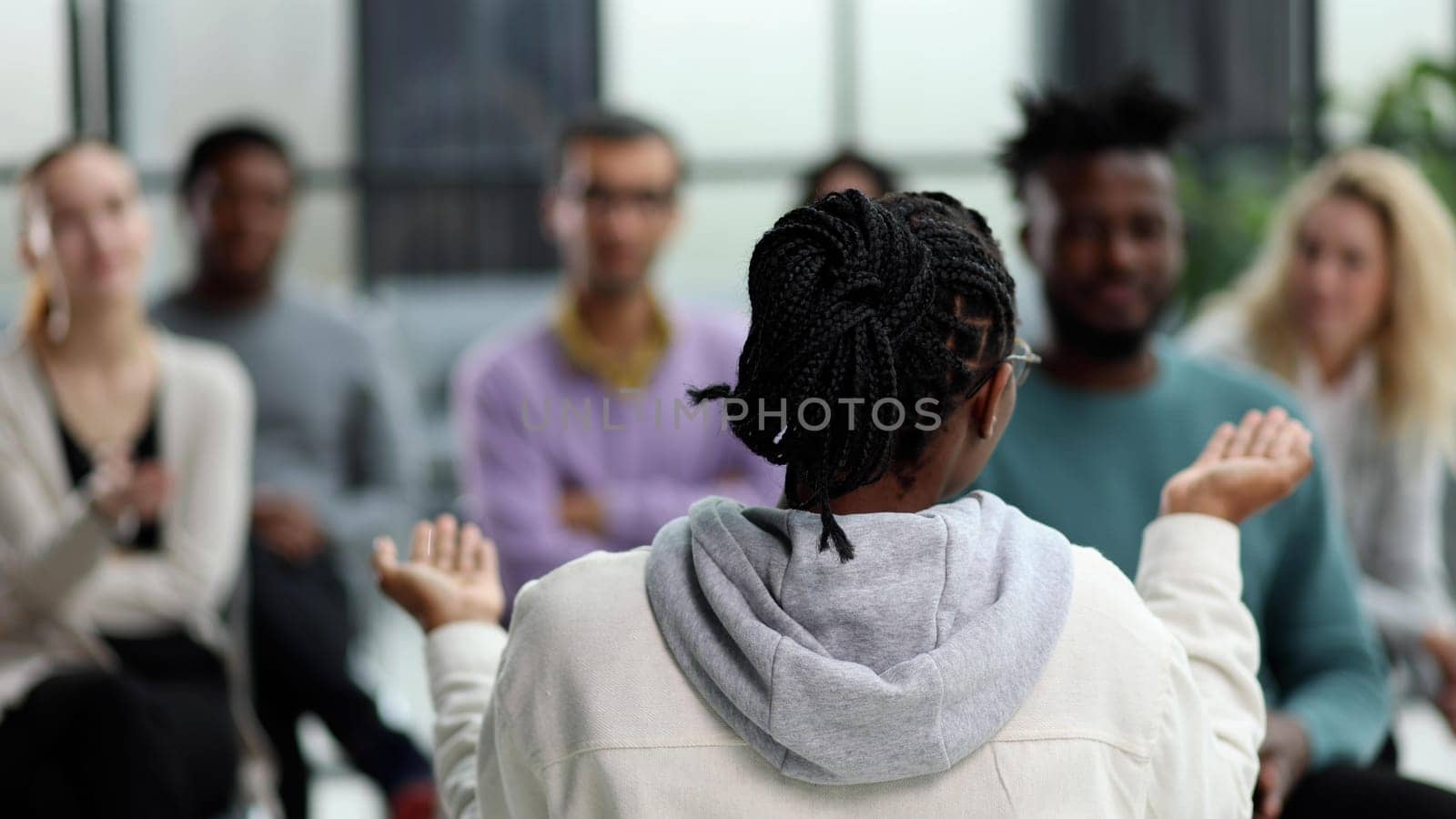 a black woman reads a business lecture to young entrepreneurs sitting on chairs. back view