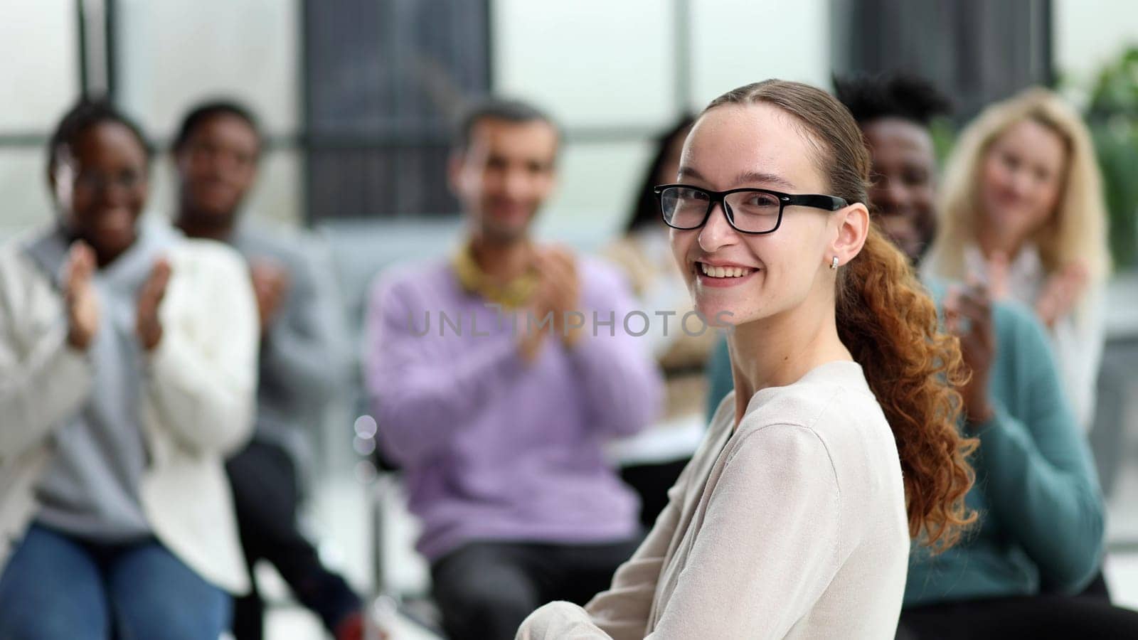 Smiling businesswoman in glasses looking at camera at a seminar with her colleagues nearby