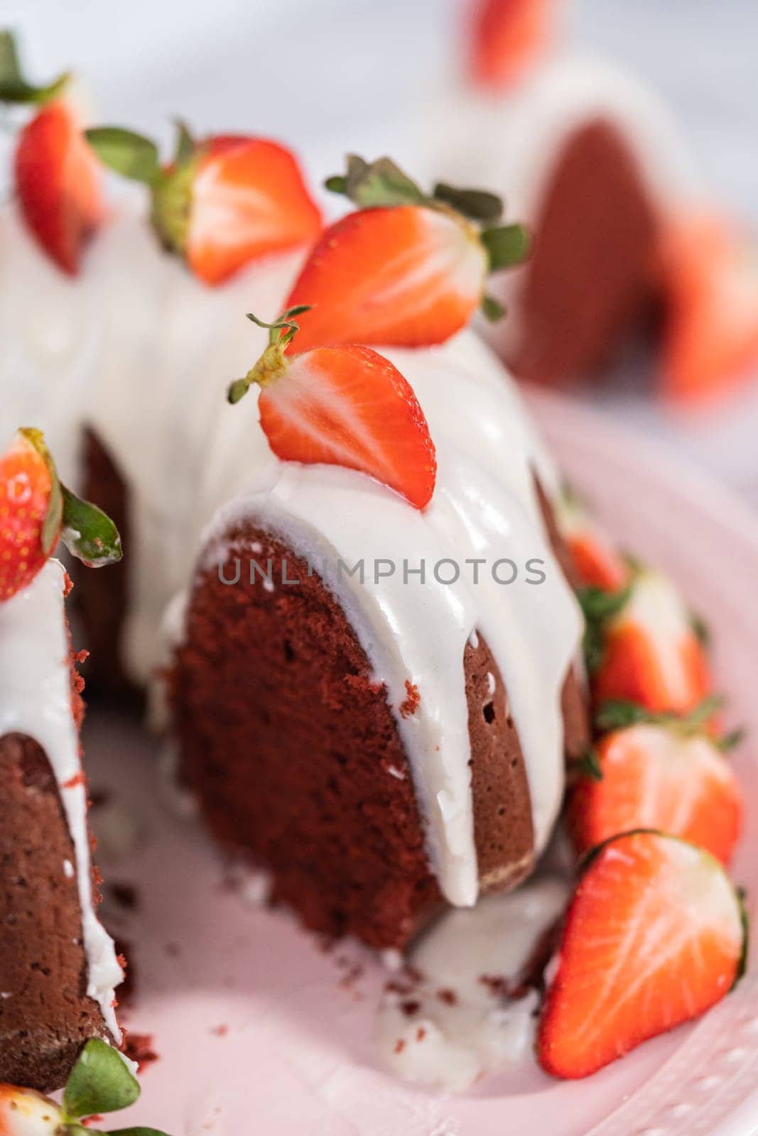 Slicing red velvet bundt cake with cream cheese frosting garnished with fresh strawberries.