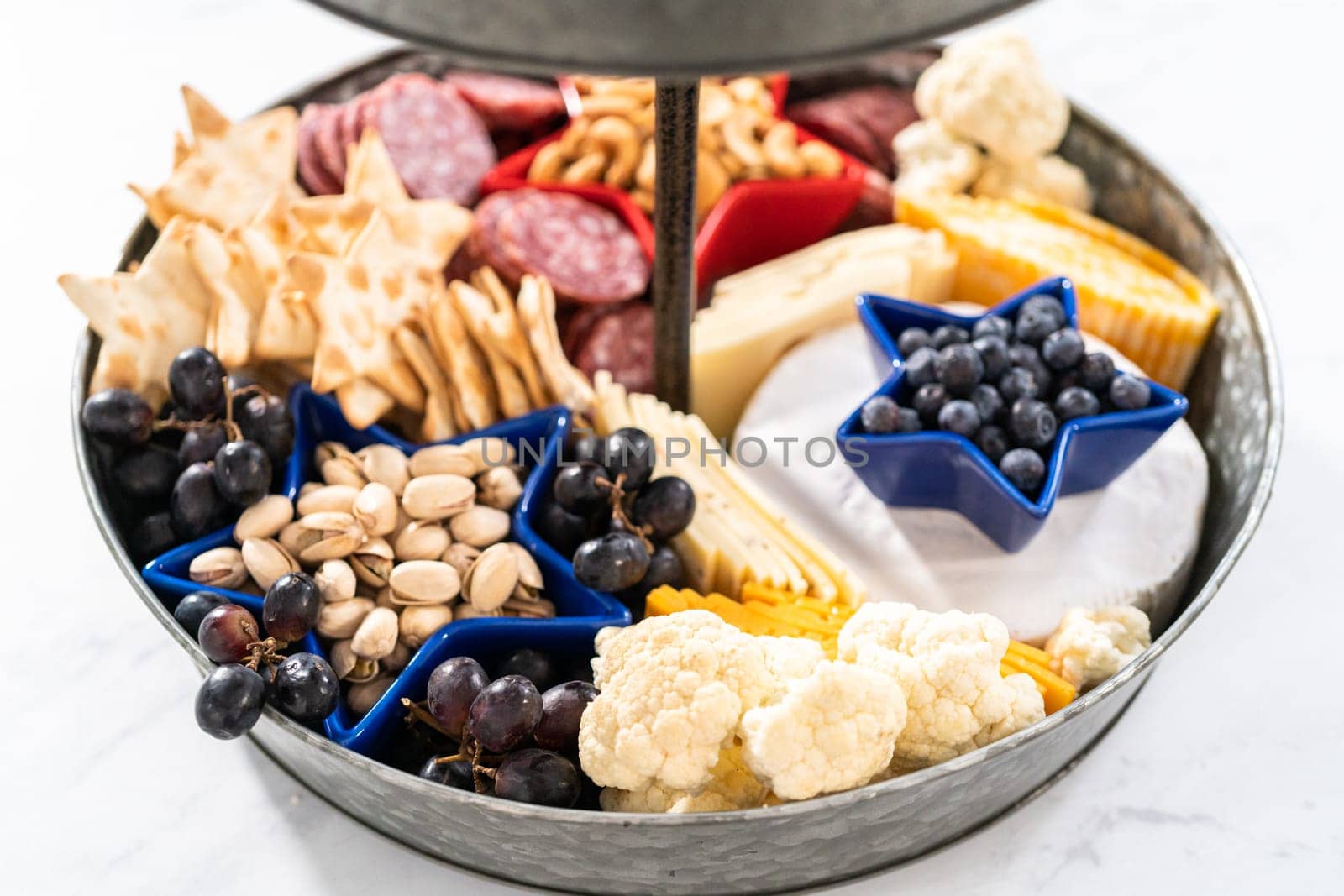 July 4th charcuterie board on a two-tiered serving metal stand filled with cheese, crackers, salami, and fresh fruits