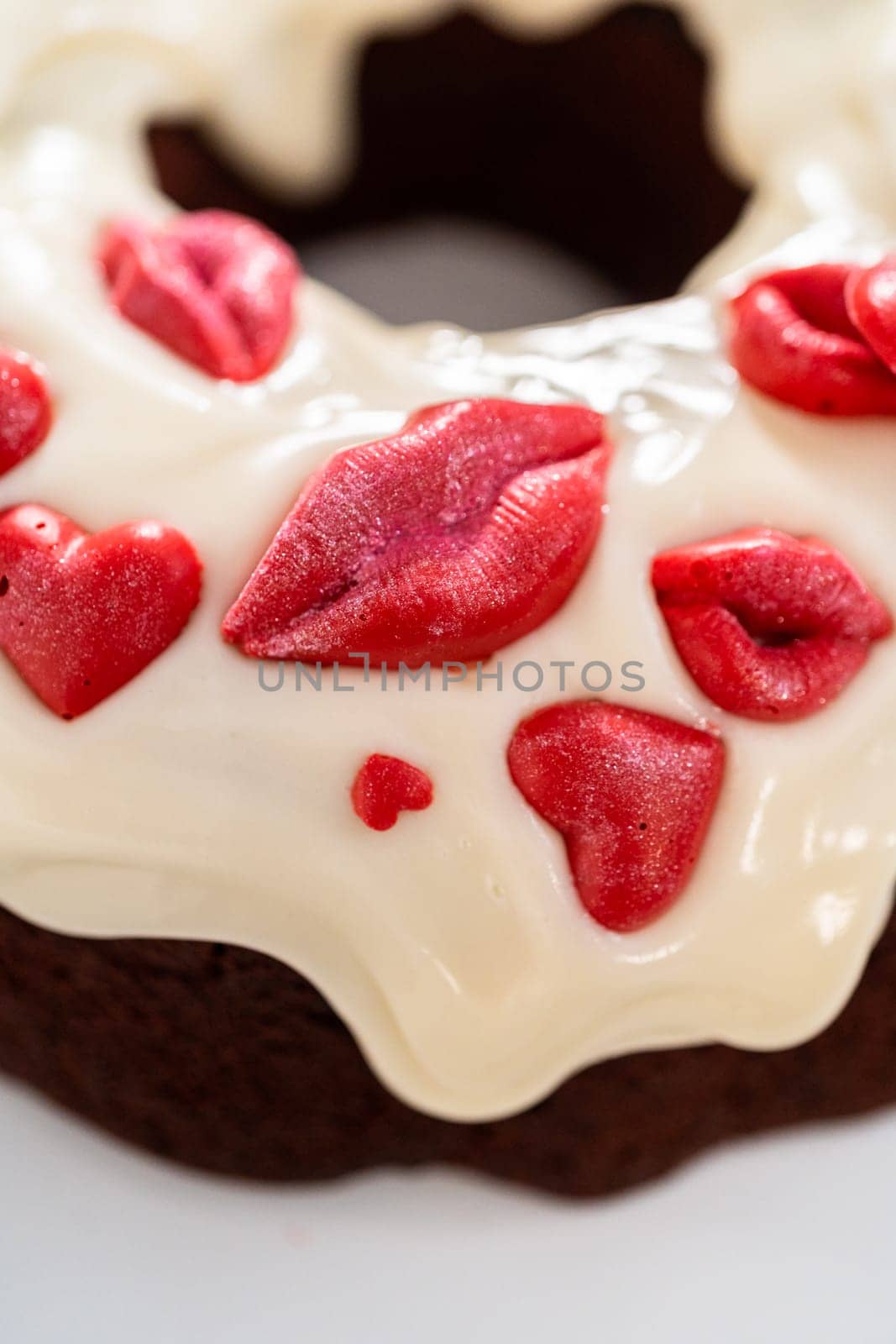 Freshly baked red velvet bundt cake with chocolate lips and hearts over cream cheese glaze for Valentine's Day.