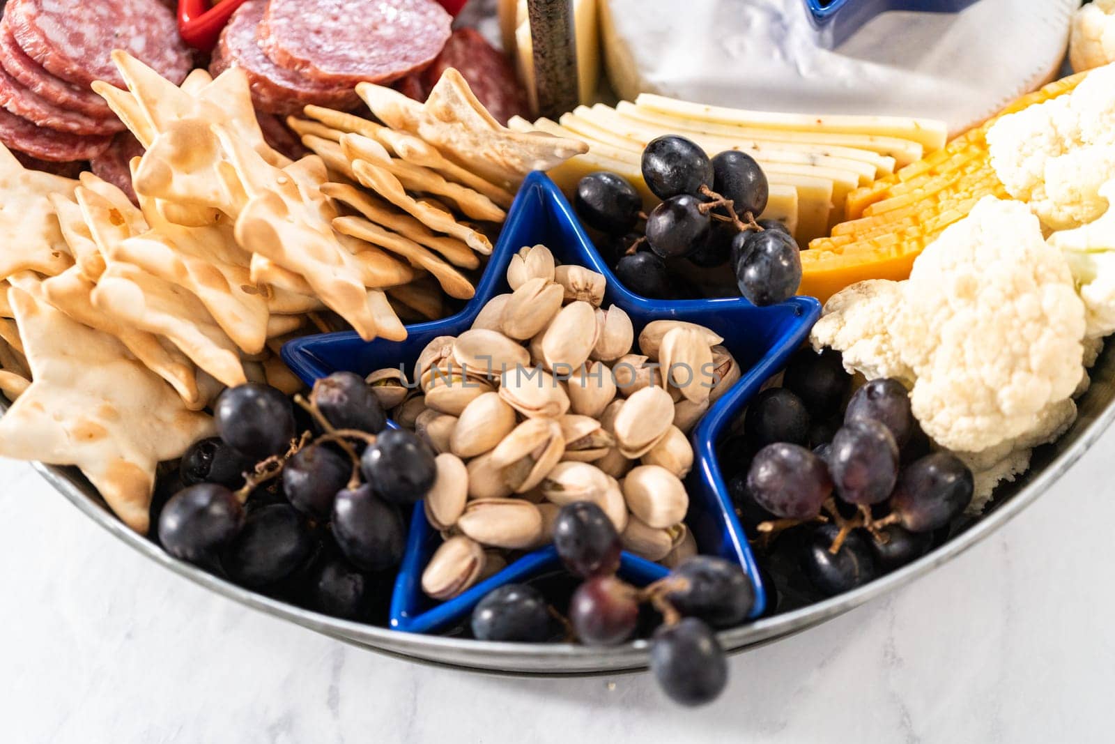 July 4th charcuterie board on a two-tiered serving metal stand filled with cheese, crackers, salami, and fresh fruits