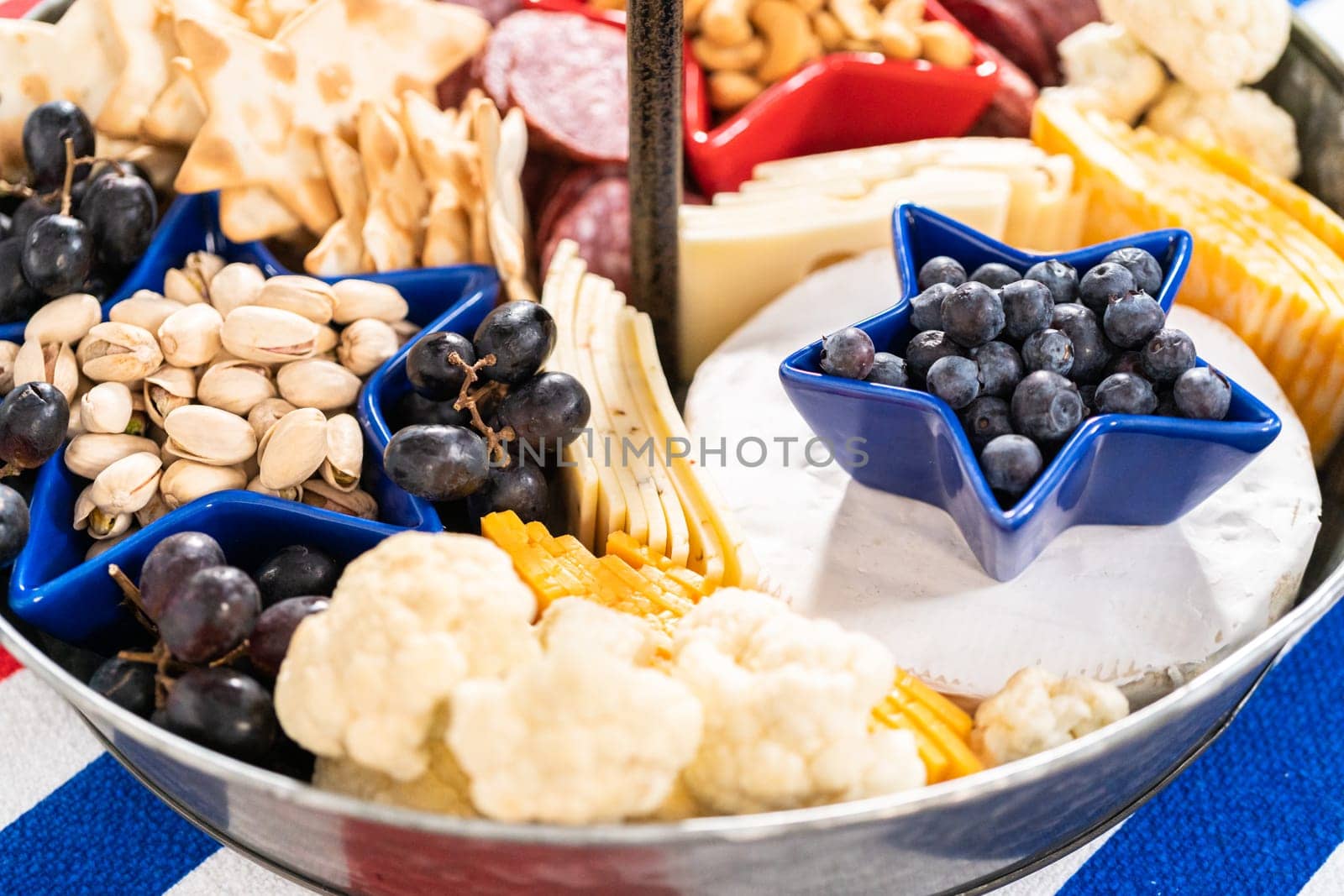 July 4th charcuterie board on a two-tiered serving metal stand filled with cheese, crackers, salami, and fresh fruits