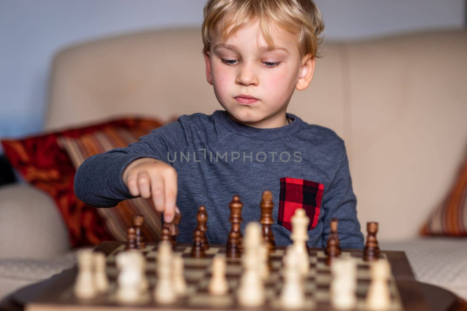 Small child 5 years old playing a game of chess on large chess board. Chess board on table in front of the boy thinking of next move, tournament