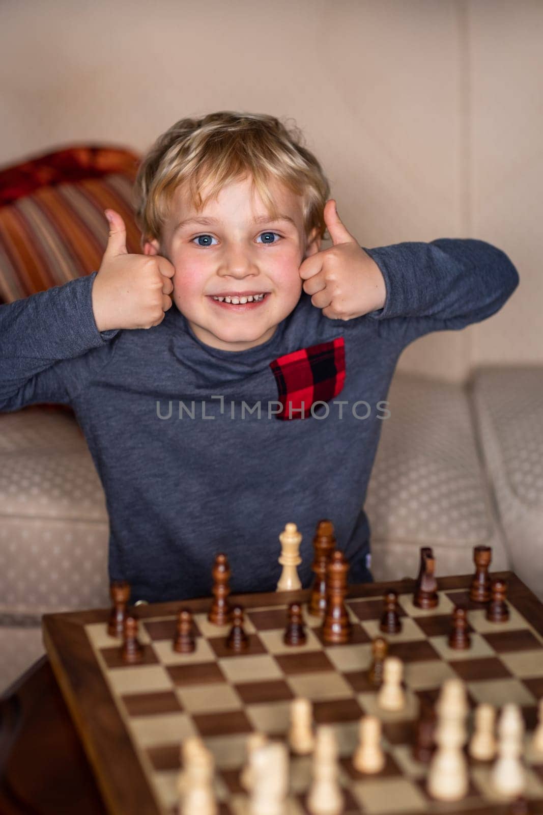 Small child 5 years old playing a game of chess on large chess board. Chess board on table in front of the boy he is happy to win, showing thumbs up