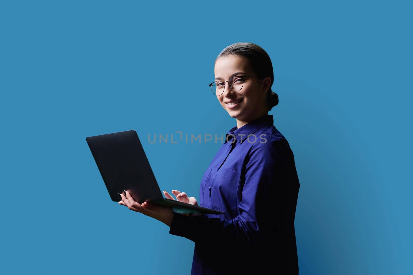 Teenage girl high school student using laptop looking at camera on blue background. Education, learning, technology, adolescence concept