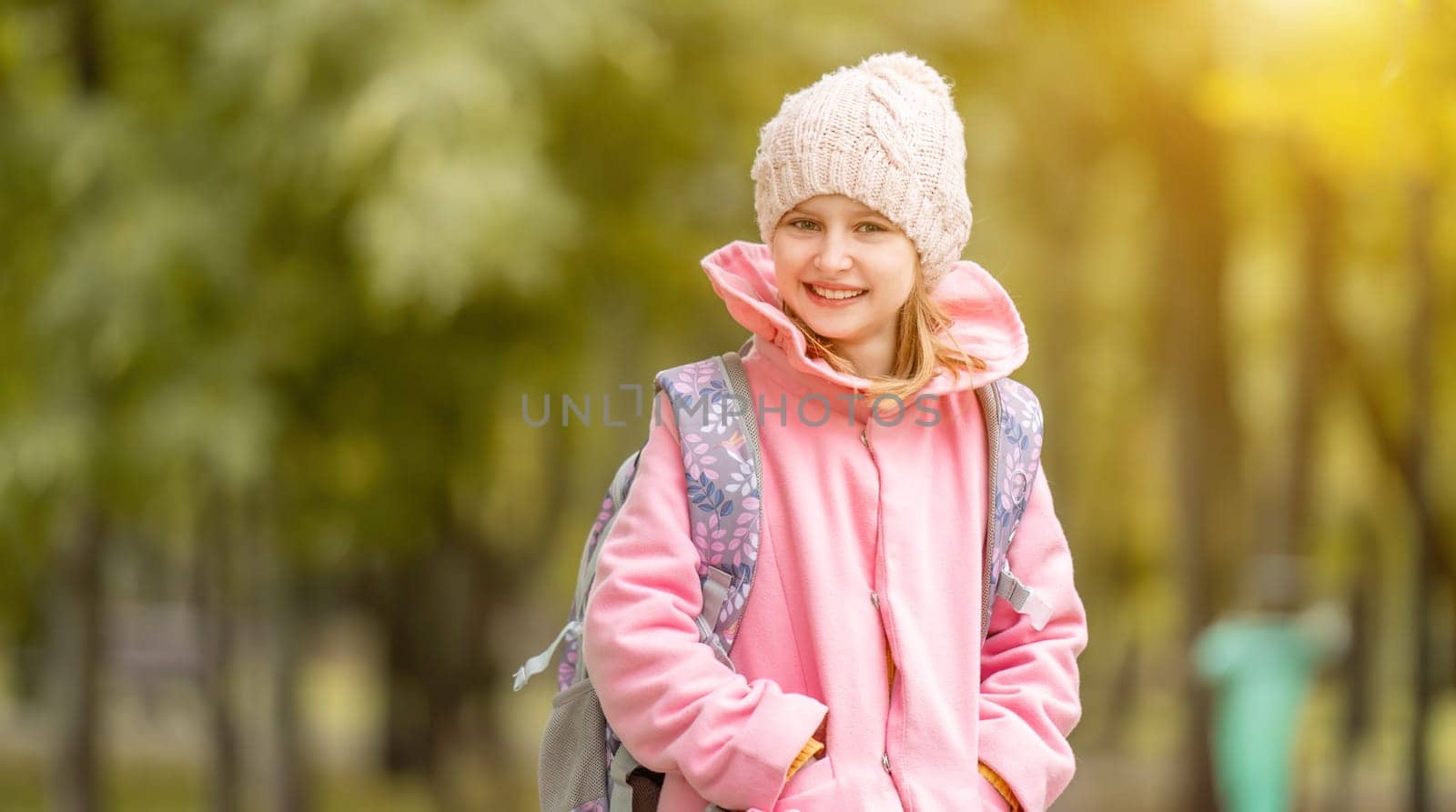 School girl with backpack smiling at autumn park and looking at camera. Preteen child portrait at street oudoors