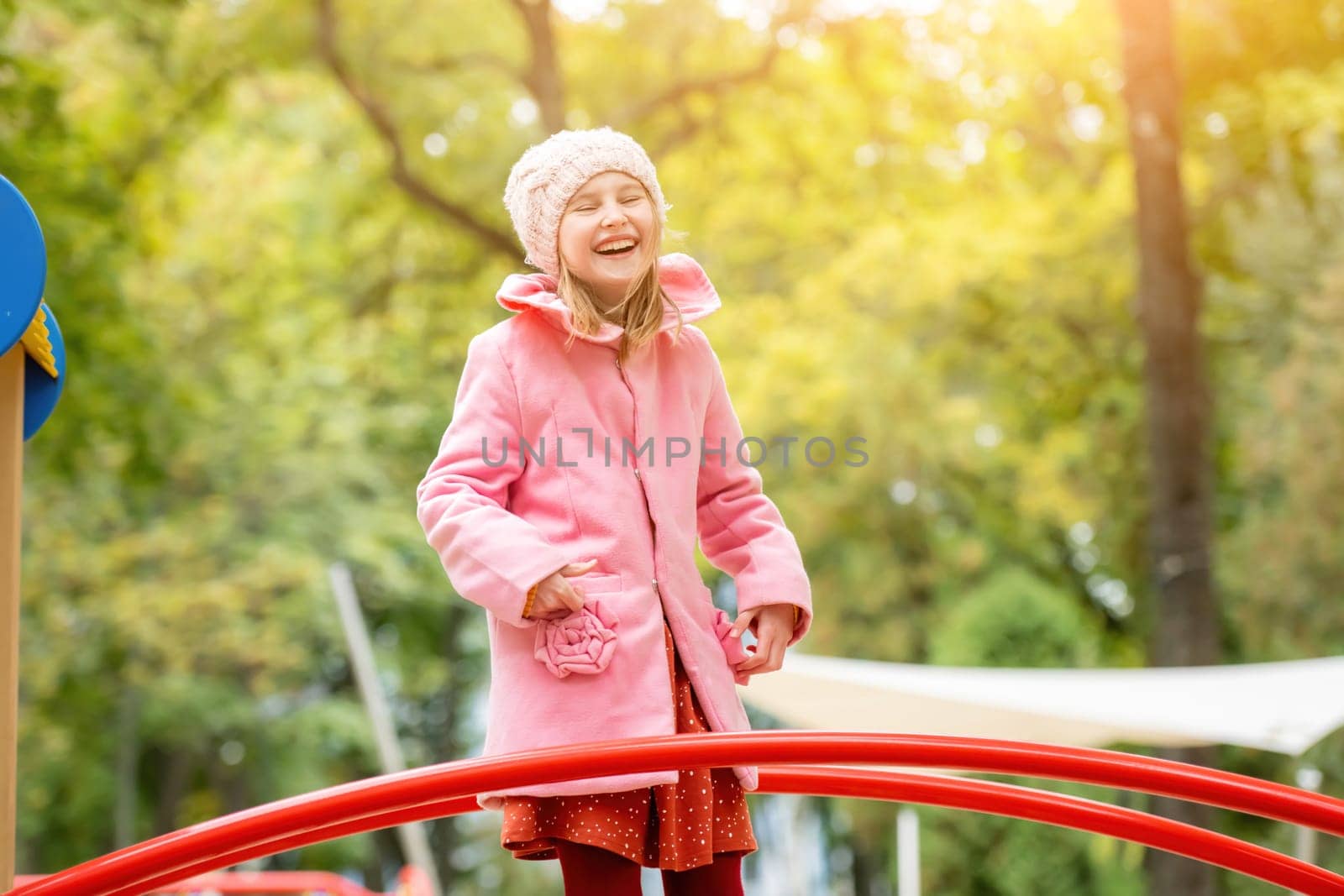 Pretty girl kid playing on playground at autumn day outdoors and laughing. Female child having fun nd smiling at the street