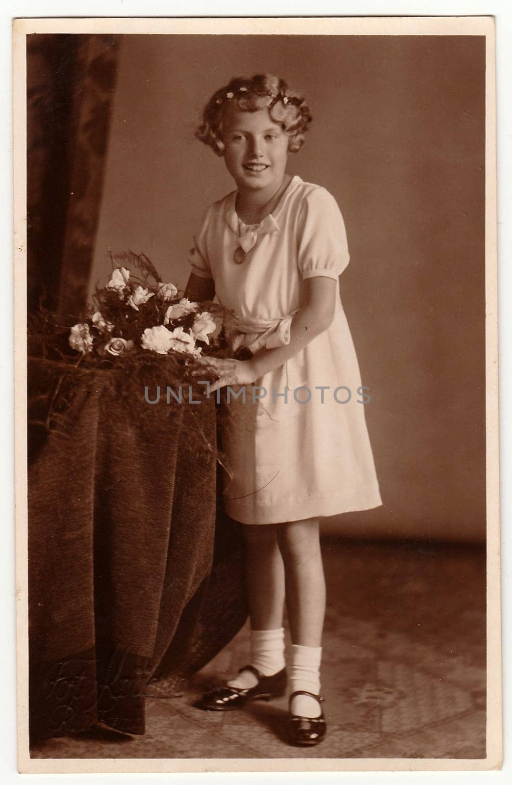 Vintage photo shows young girl with bouquet poses in a photography studio. Photo with dark sepia tint. Black white studio portrait. by roman_nerud