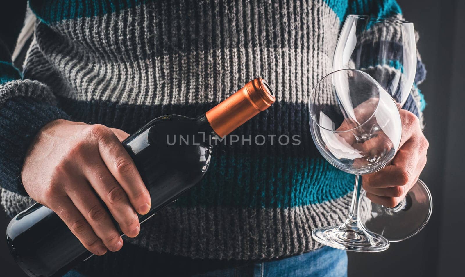 Man holding wine bottle and glasses closeup on black background. Guy with grape alcohol beverage and wineglasses