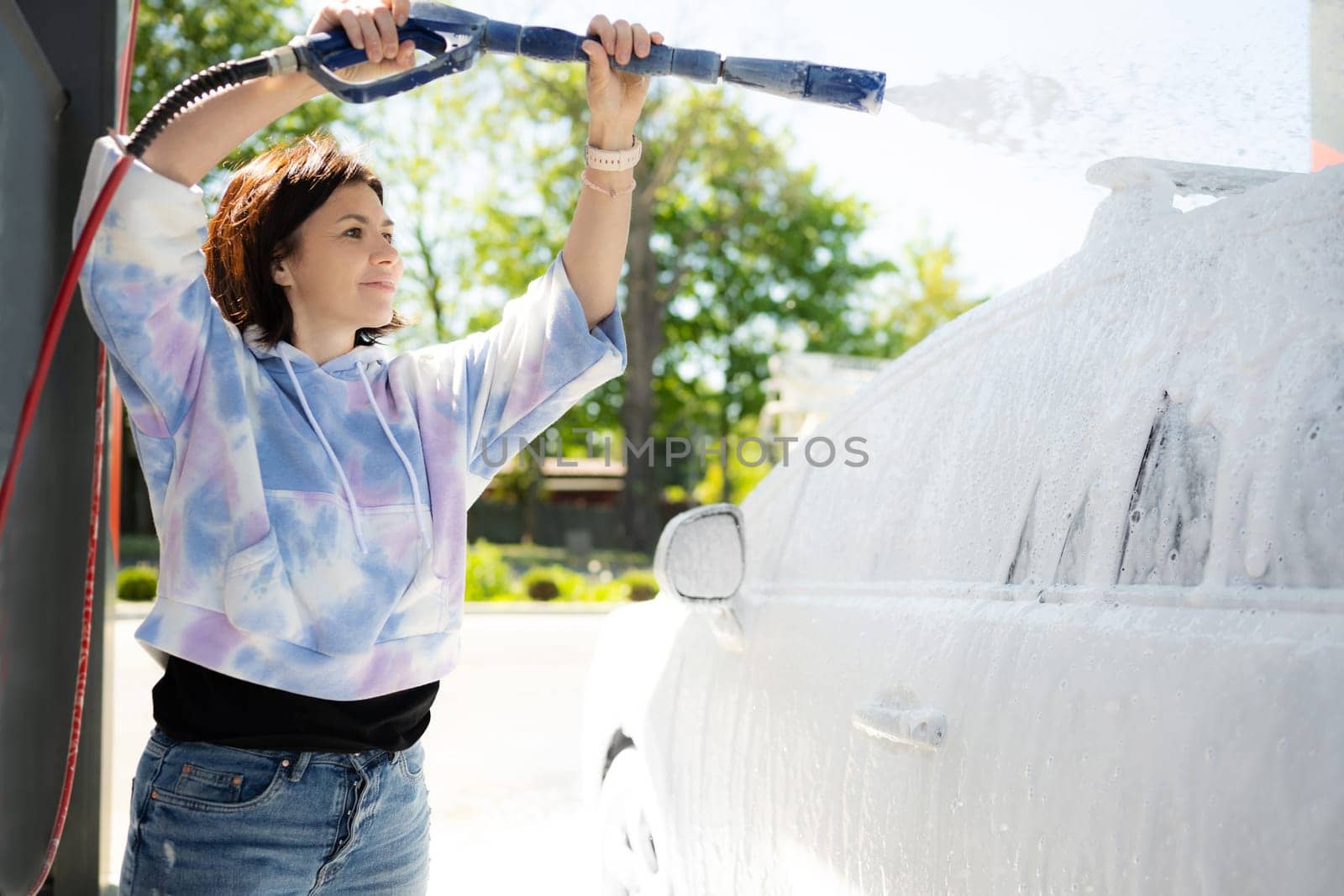 Girl washing a car in a self-service car wash station with wahing foam. Wash car self-service station.