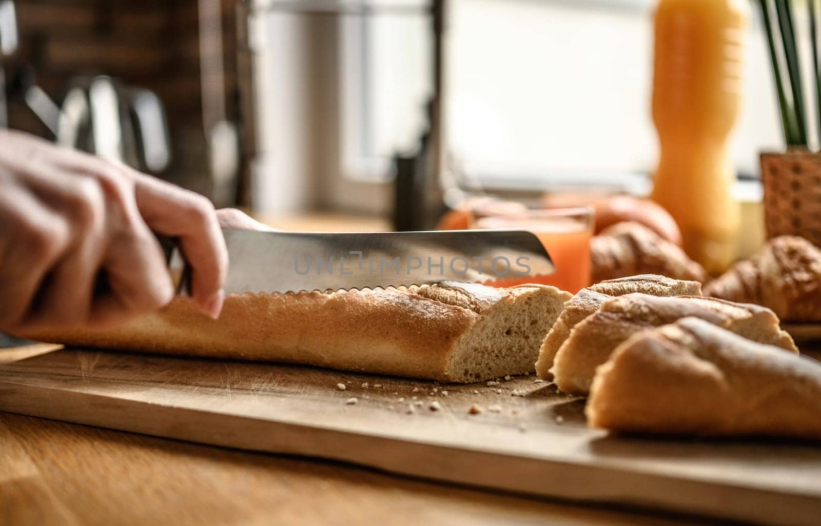 Woman cutting fresh baguette on a cutting board at the kitchen. Cooking fresh french breakfast.