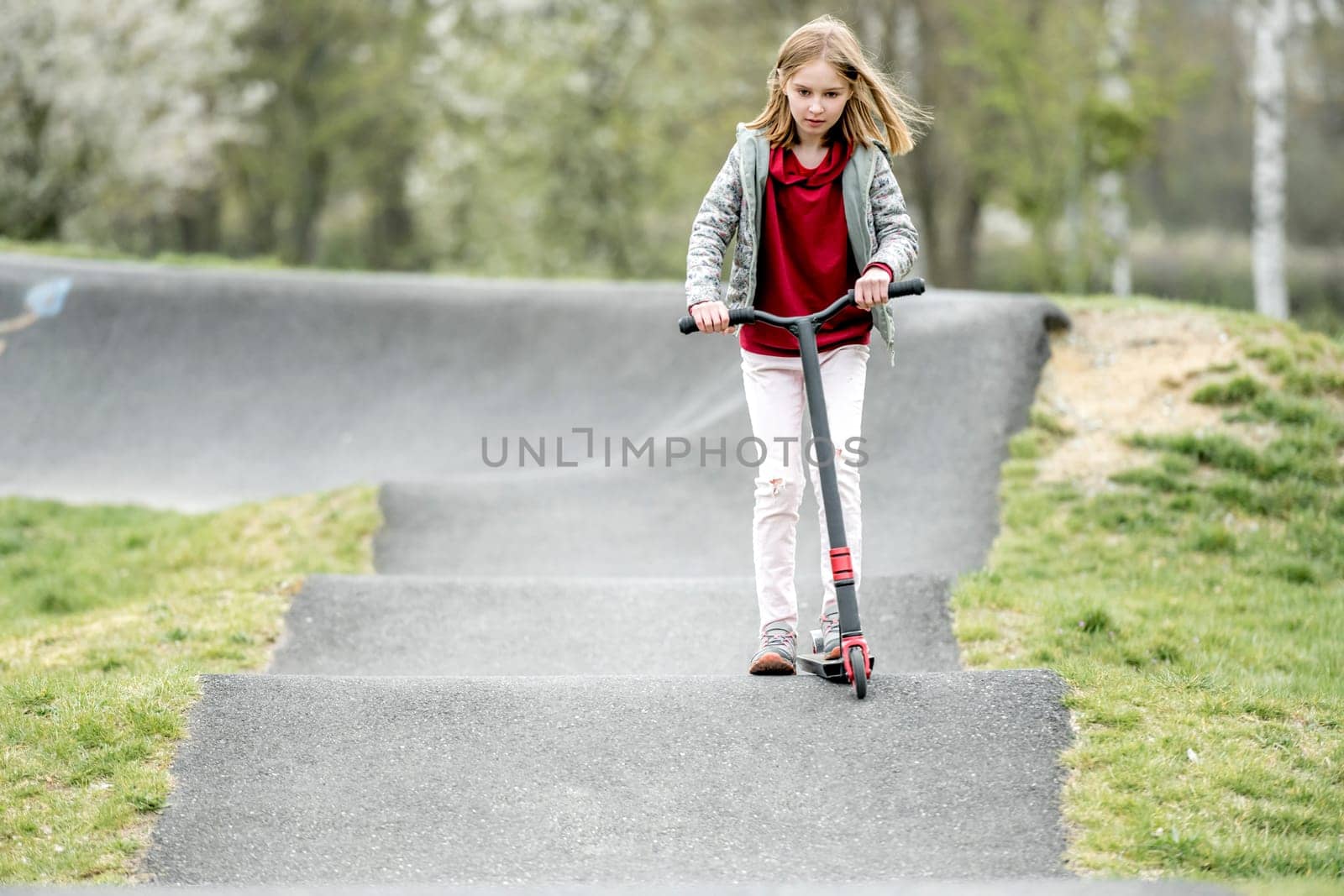 Beautiful little girl rides a scooter in a extreme ride park