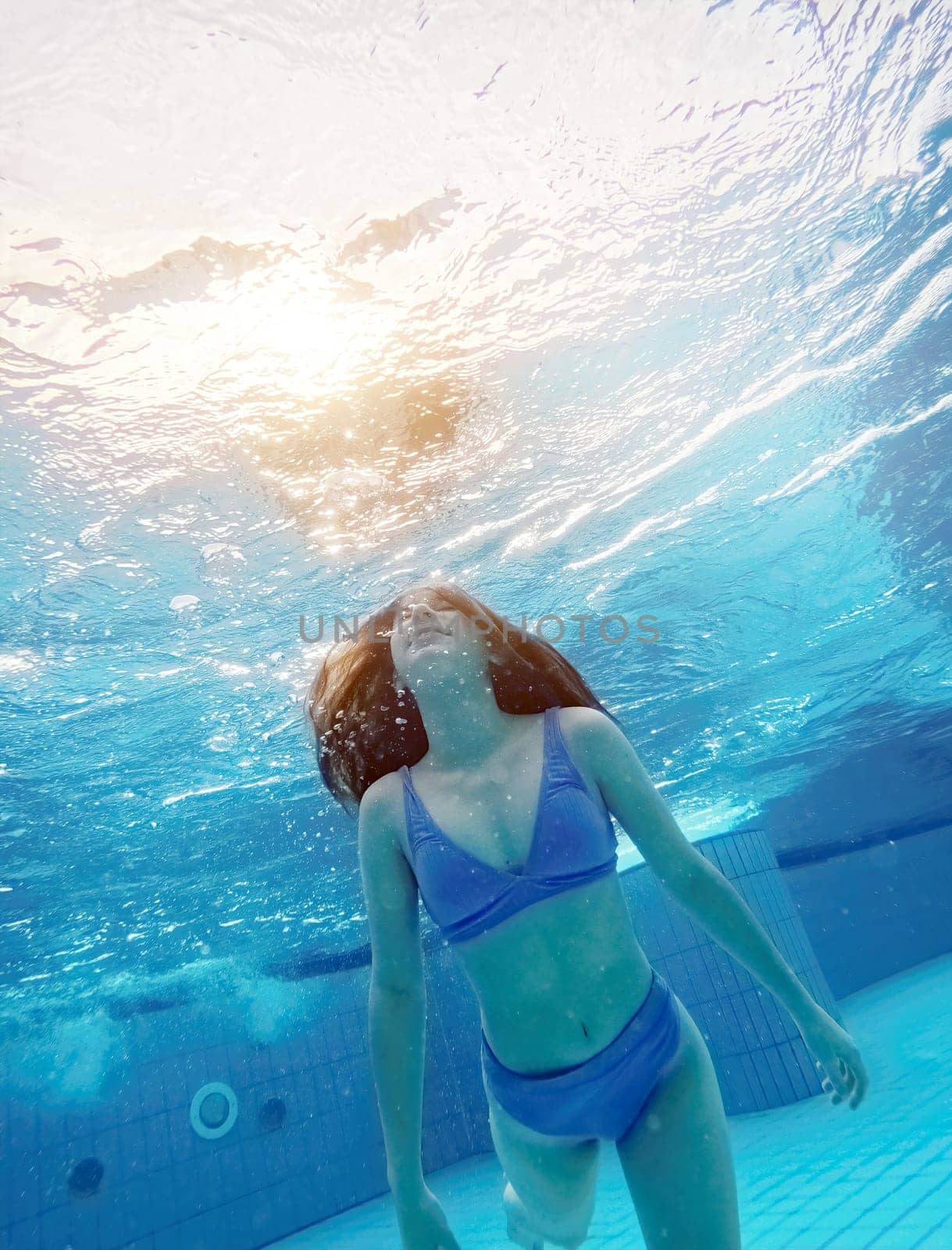 Teen girl swimming under water in blue pool by GekaSkr