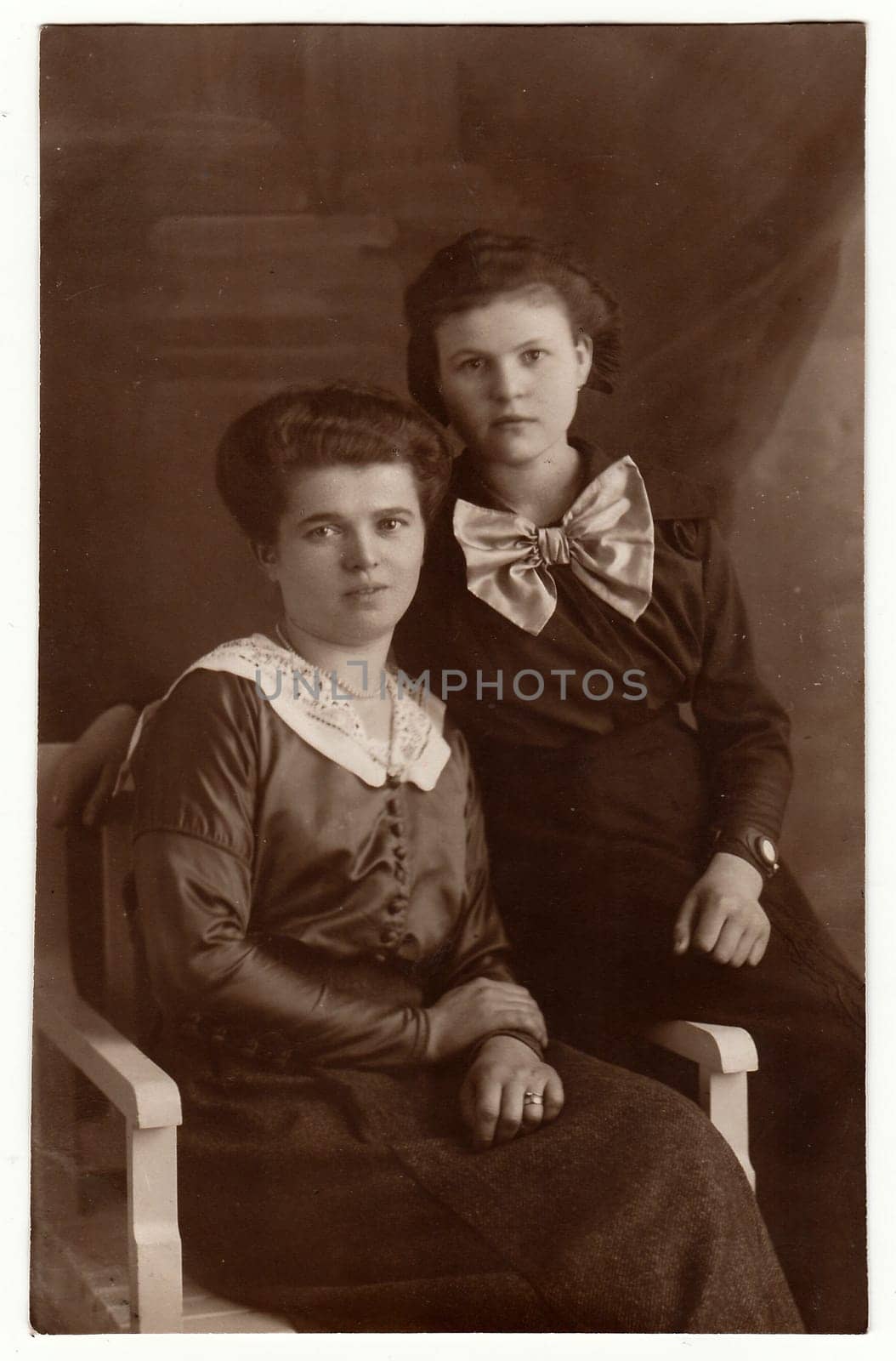 BERLIN, GERMANY - 1919: Vintage photo shows mature woman and her daughter pose in a photography studio. Black white antique studio portrait.