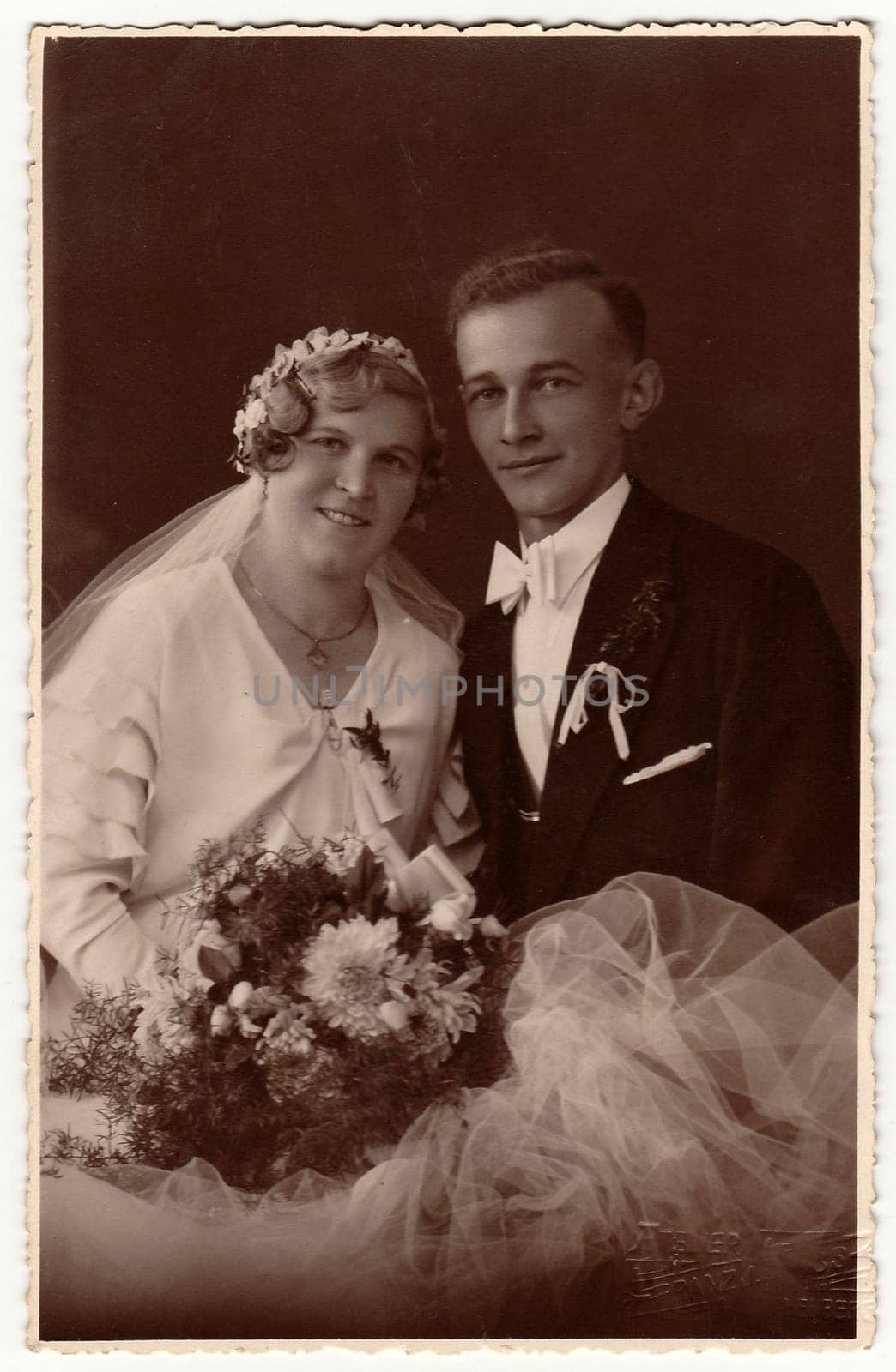 Vintage photo of newlyweds with wedding bouquet. Bride wears wedding veil headdress. Groom wears posh clothing, white bow-tie. Black white antique studio portrait. by roman_nerud