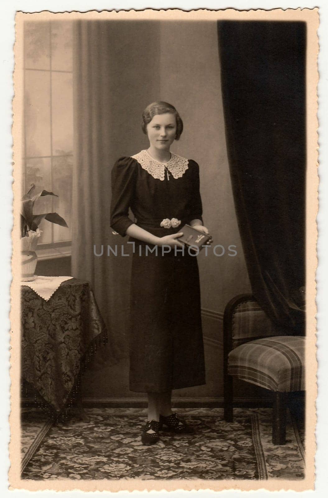 Vintage photo shows an elegant woman with book poses in a photography studio. Photo with dark sepia tint. Black white studio portrait. by roman_nerud