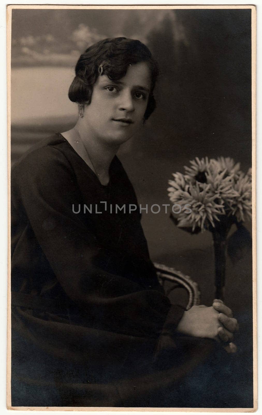 Vintage photo shows a woman with bouquet poses in a photography studio. Photo with sepia tint. Black white studio portrait. by roman_nerud