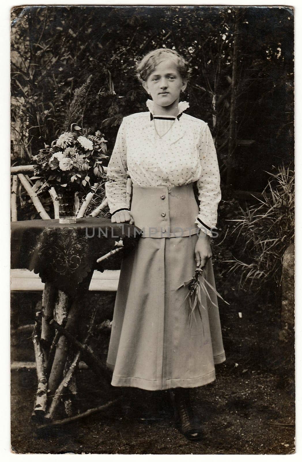 Vintage photo shows an elegant woman poses next to a rustic garden table. Black white antique photo. by roman_nerud