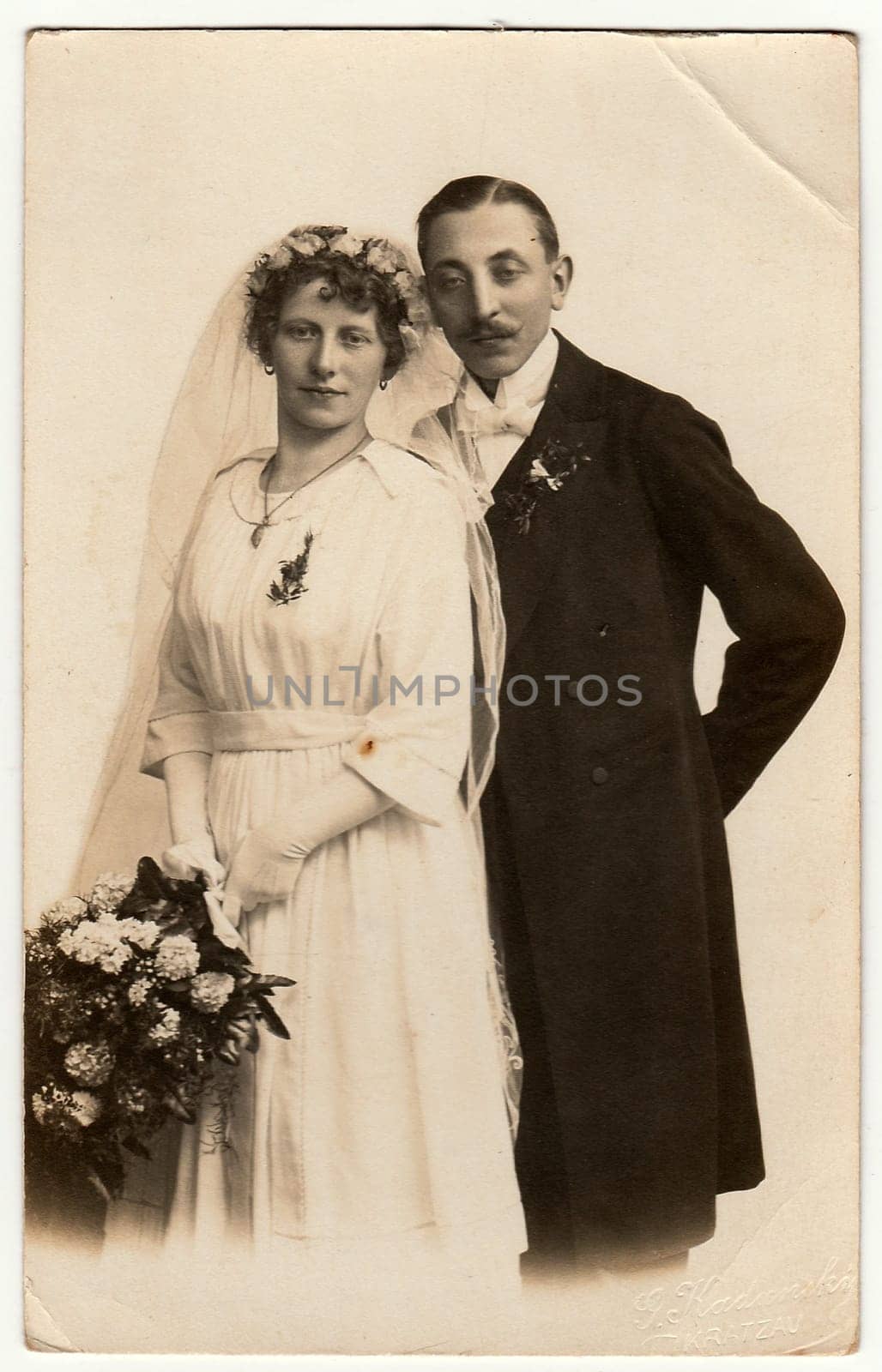 Vintage photo of newlyweds with wedding bouquet. Bride wears wedding veil headdress. Groom wears posh clothing, white bow-tie. Black white antique studio portrait. by roman_nerud