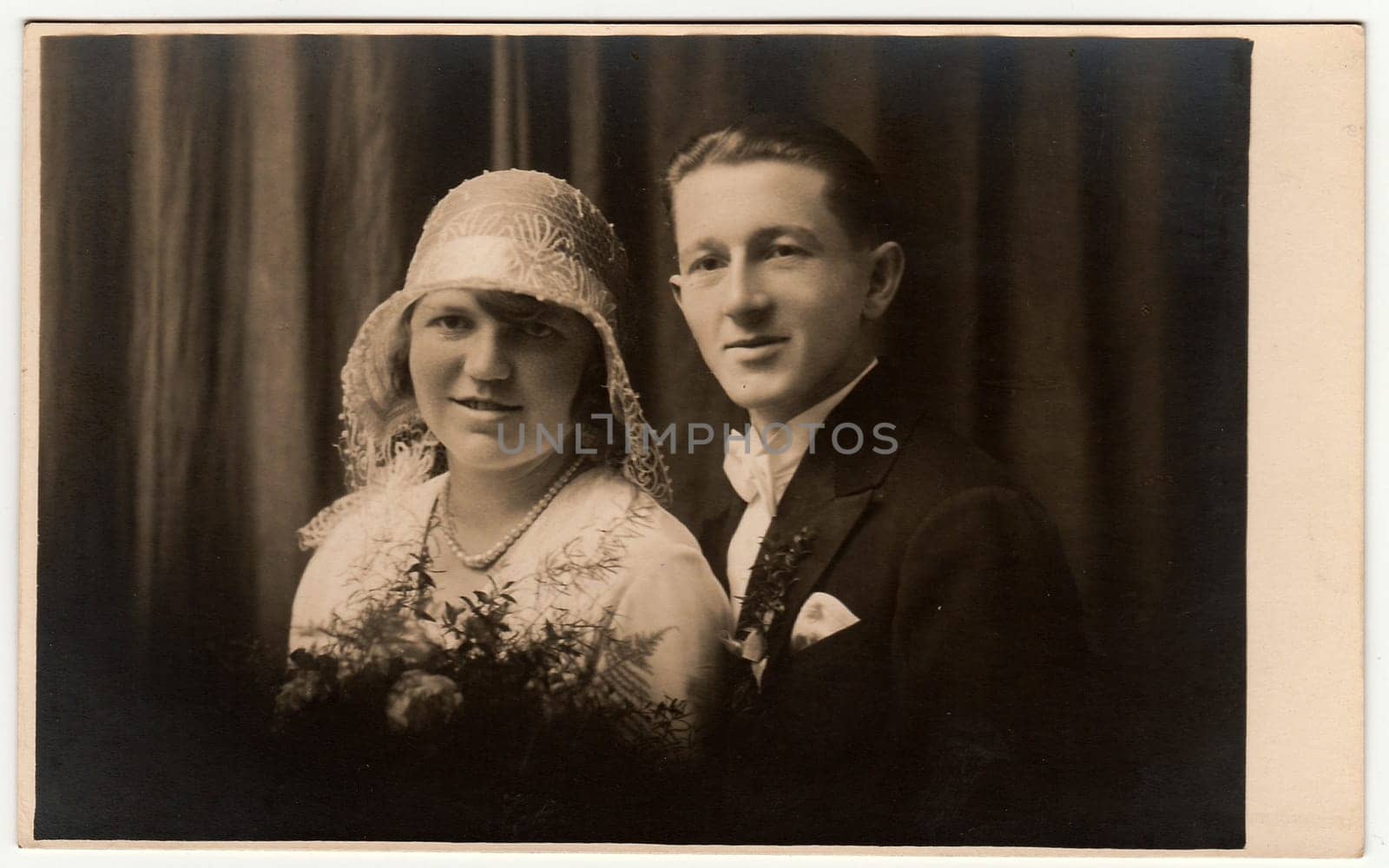 Vintage photo of newlyweds. Bride wears white hat with lace bobbin . Groom wears posh clothing, white bow-tie. Black white antique studio portrait. by roman_nerud