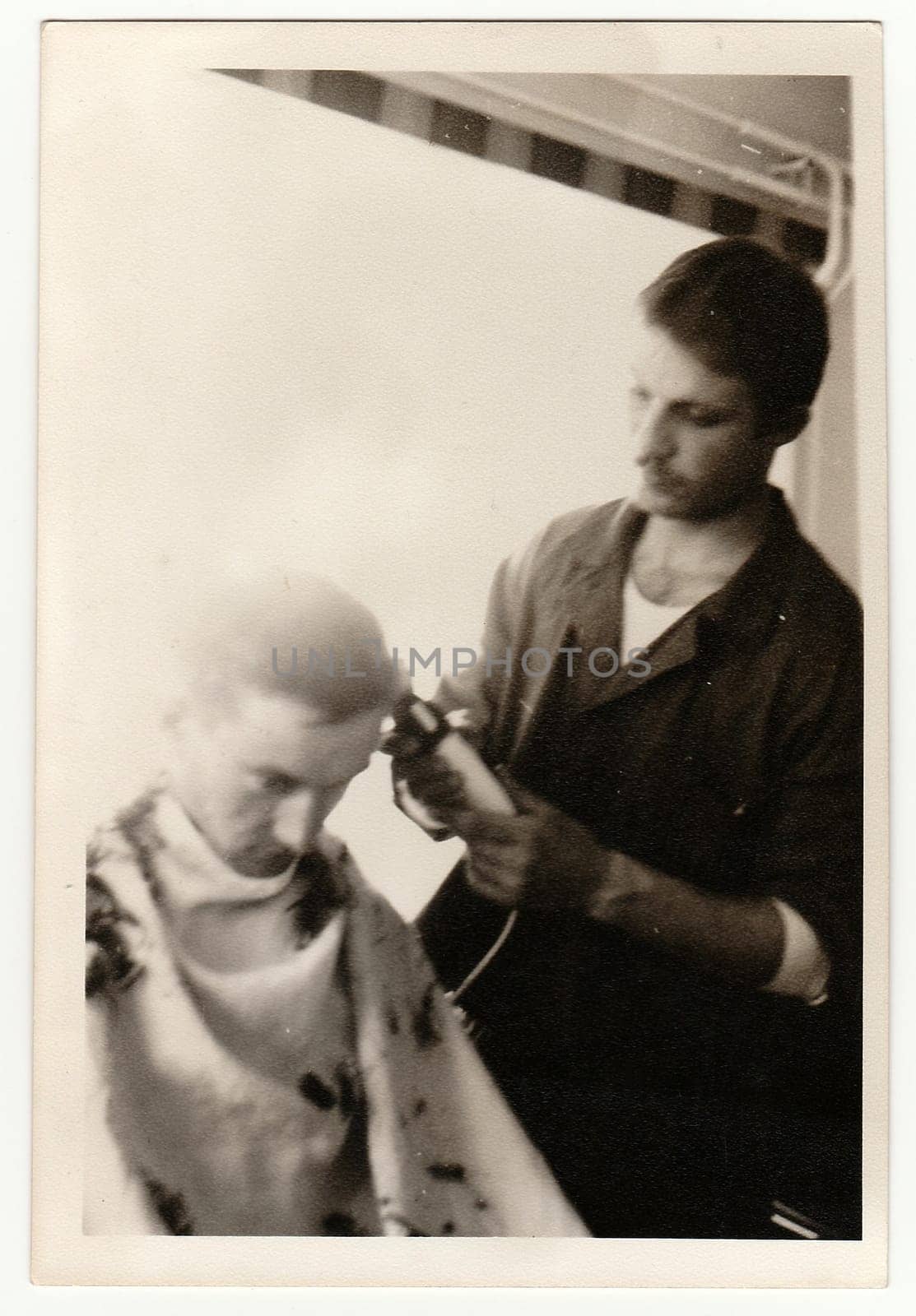 Vintage photo shows young man shaves a new soldier head clean. Antique black & white photography. by roman_nerud