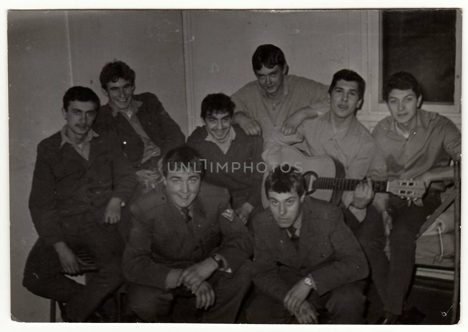 Vintage photo shows soldiers pose in barracks. One of them plays the guitar. Black & white antique photo. by roman_nerud