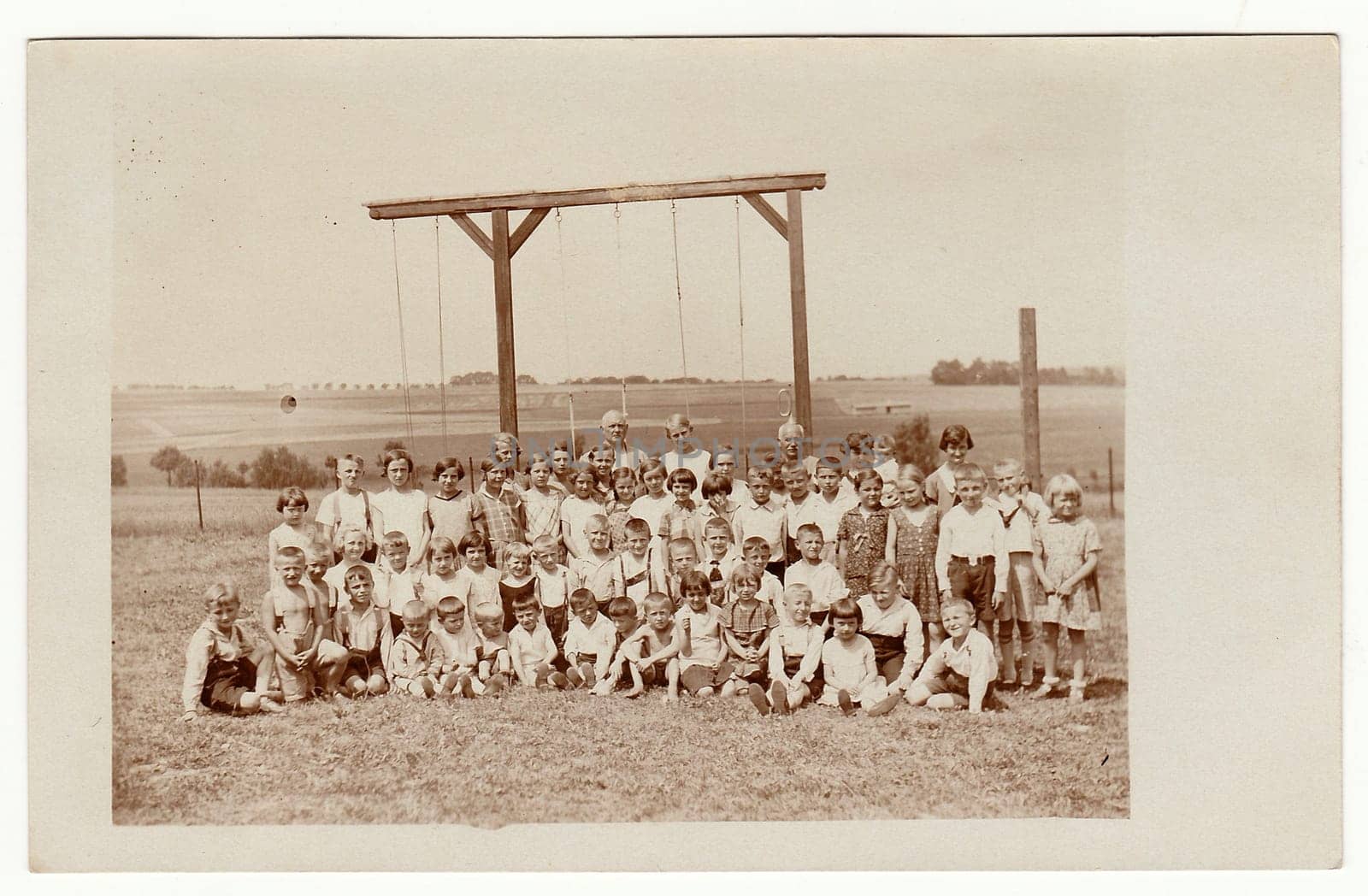 THE CZECHOSLOVAK REPUBLIC - JUNE 15, 1930: Vintage photo shows a group of children outdoors. Horizontal bar for rope - climbing is on the background. Black white photo.