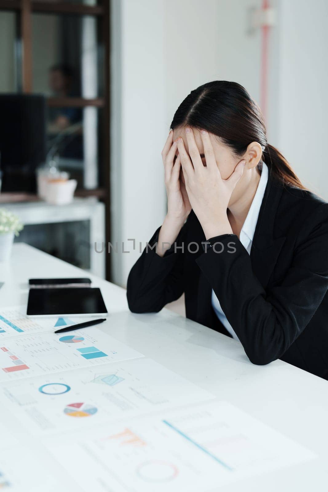 A portrait of a beautiful Asian female employee showing a stressed face while using financial documents on her desk.