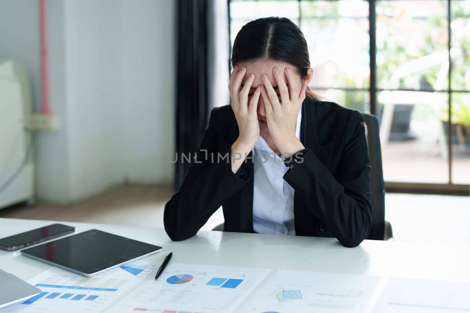 A portrait of a beautiful Asian female employee showing a stressed face while using financial documents on her desk.