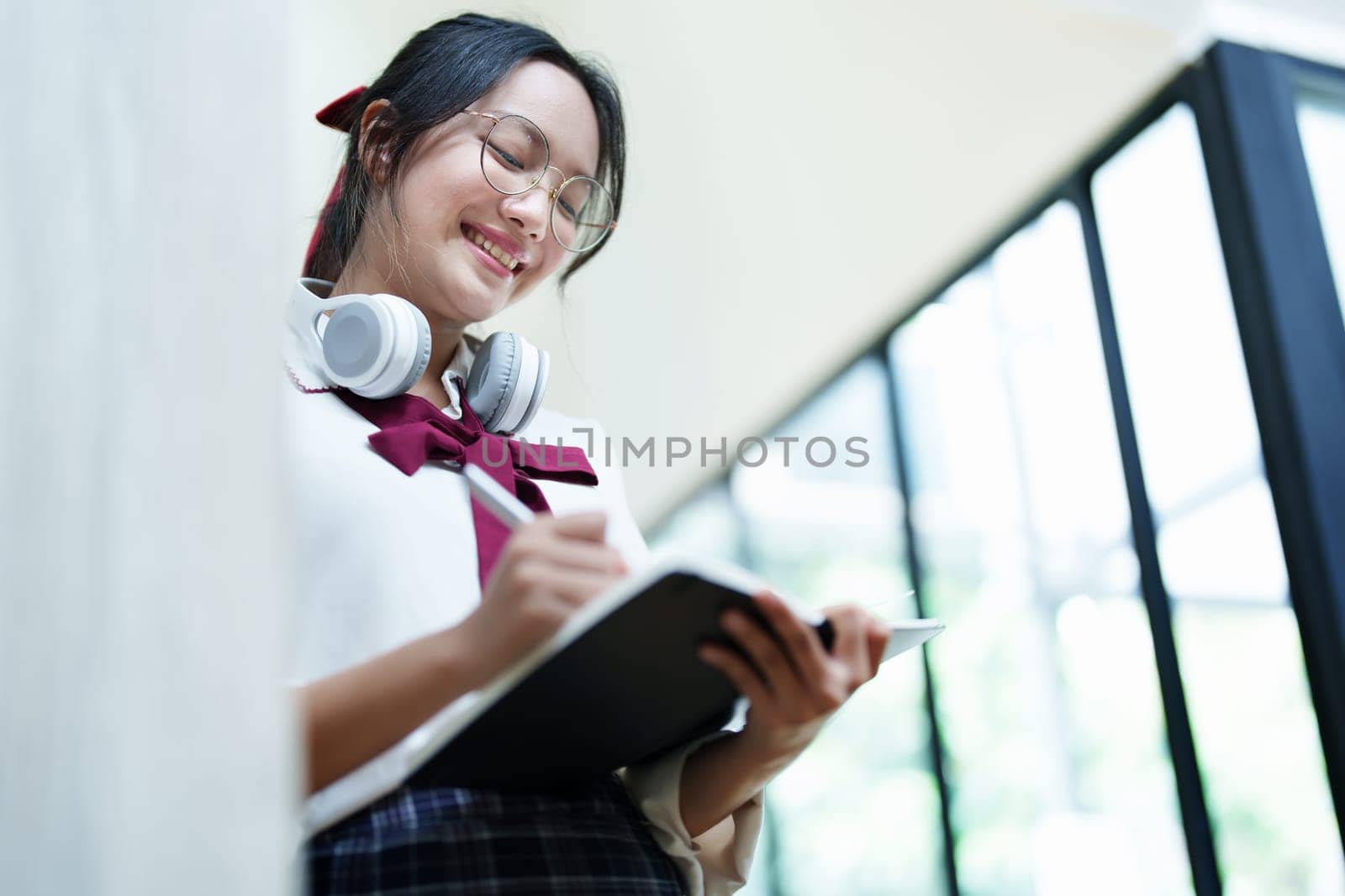 Portrait of a beautiful young Asian student using a notebook to take notes in the library.