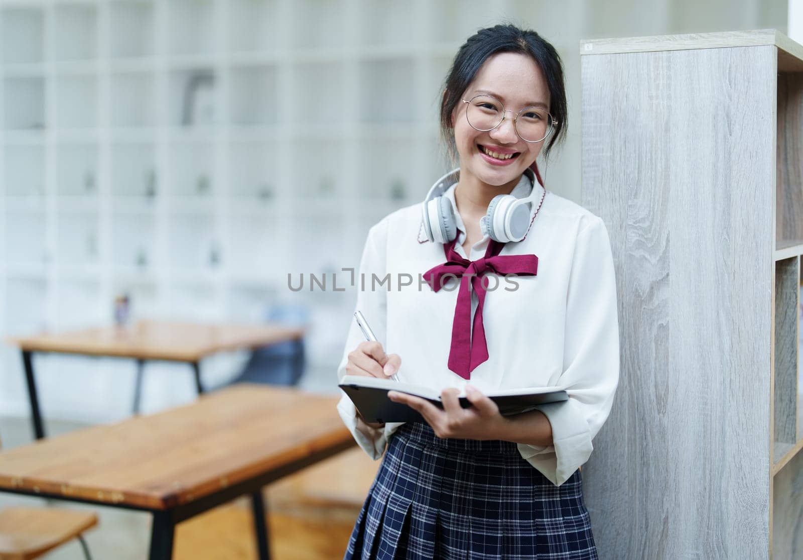 Portrait of a beautiful young Asian student using a notebook to take notes in the library.