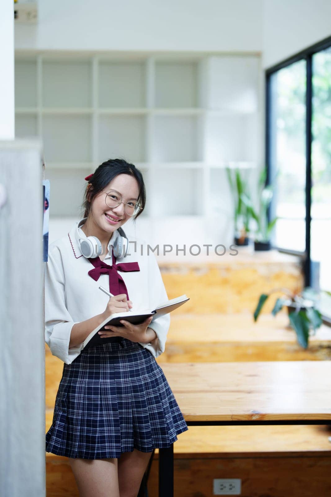 Portrait of a beautiful young Asian student using a notebook to take notes in the library by Manastrong