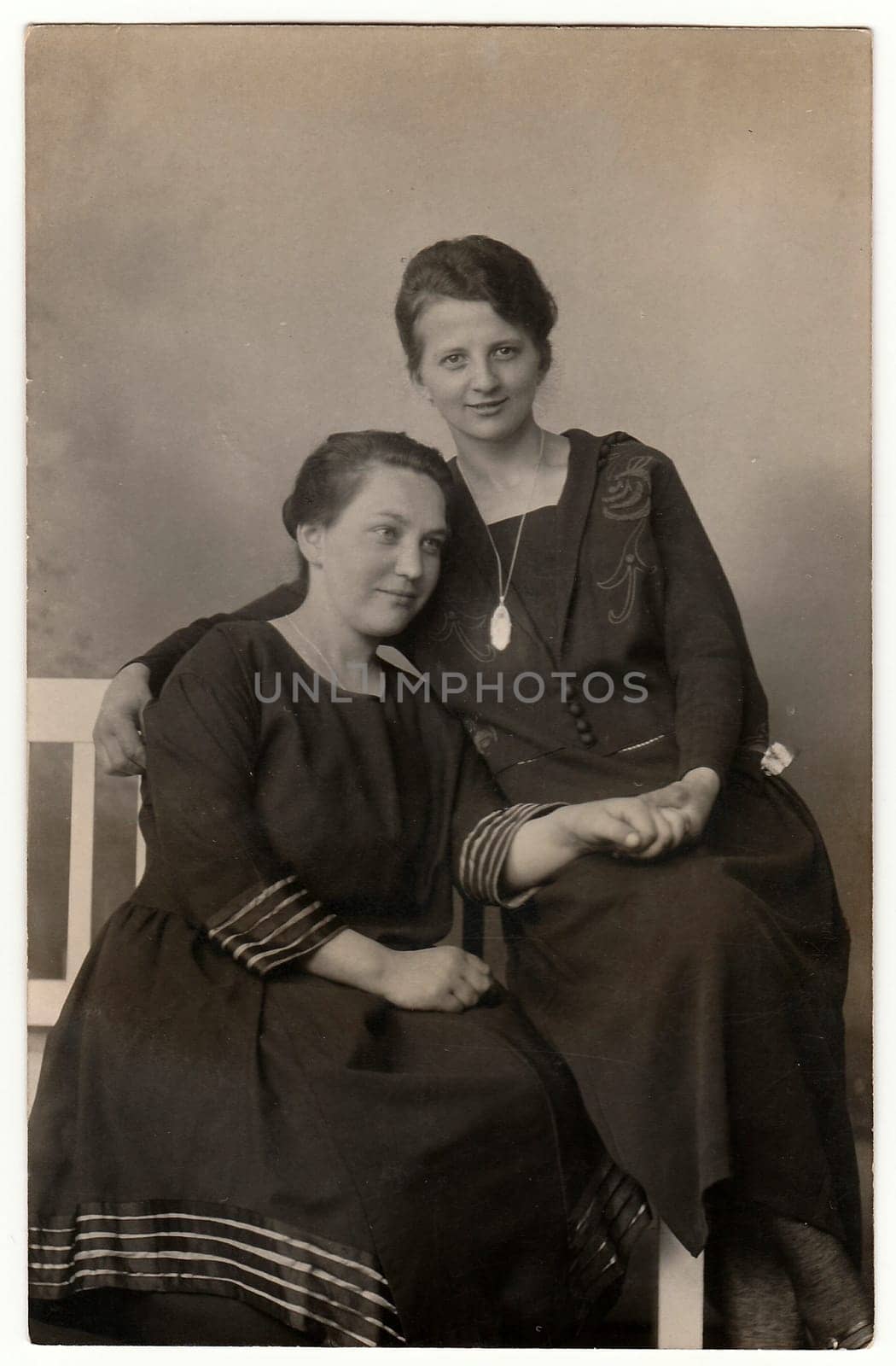 Vintage photo shows women pose in photo studio. They sit on white historic bench. Black white antique photography. by roman_nerud