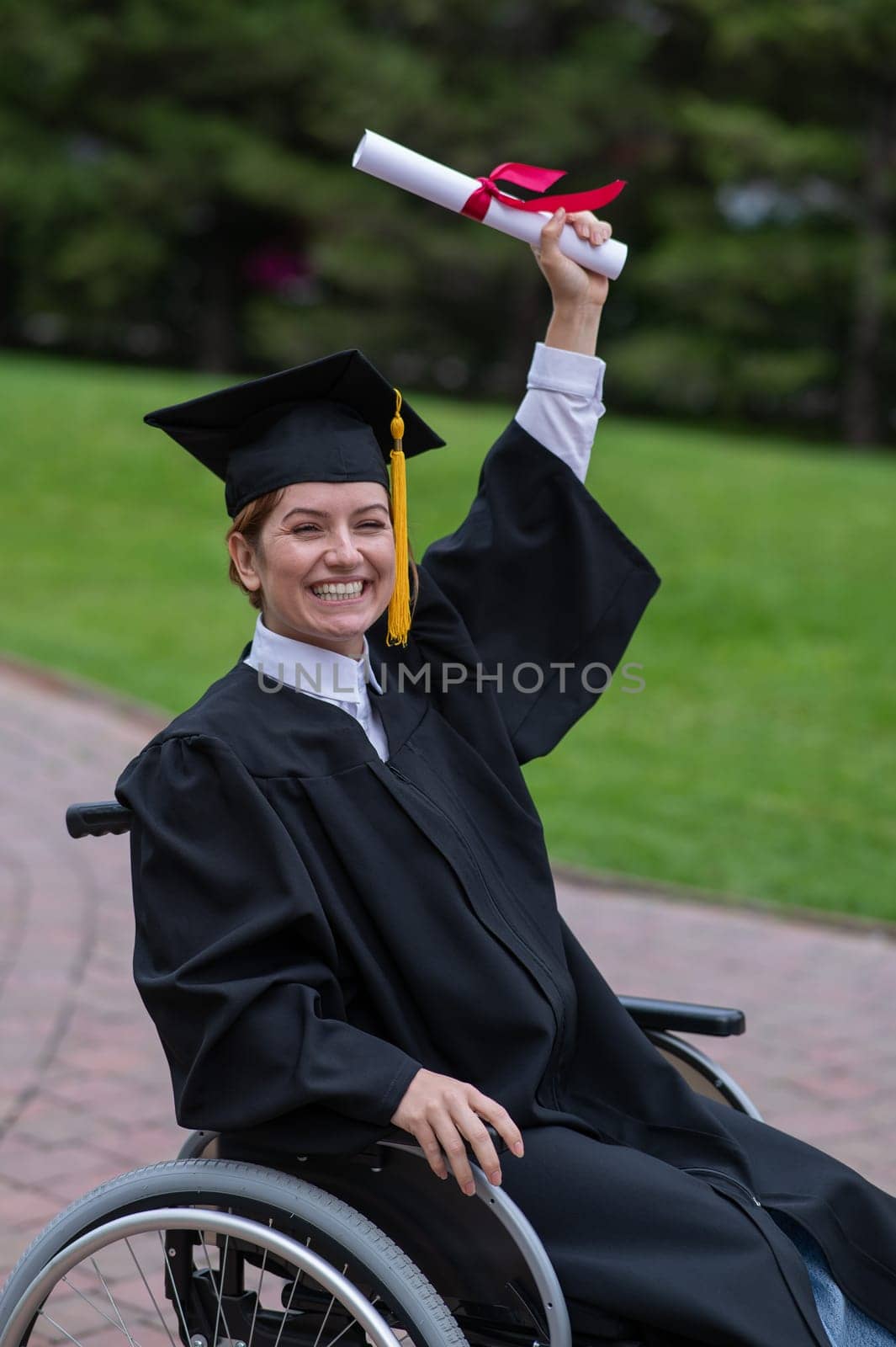 Caucasian woman in a wheelchair in a graduate costume rejoices at receiving a diploma